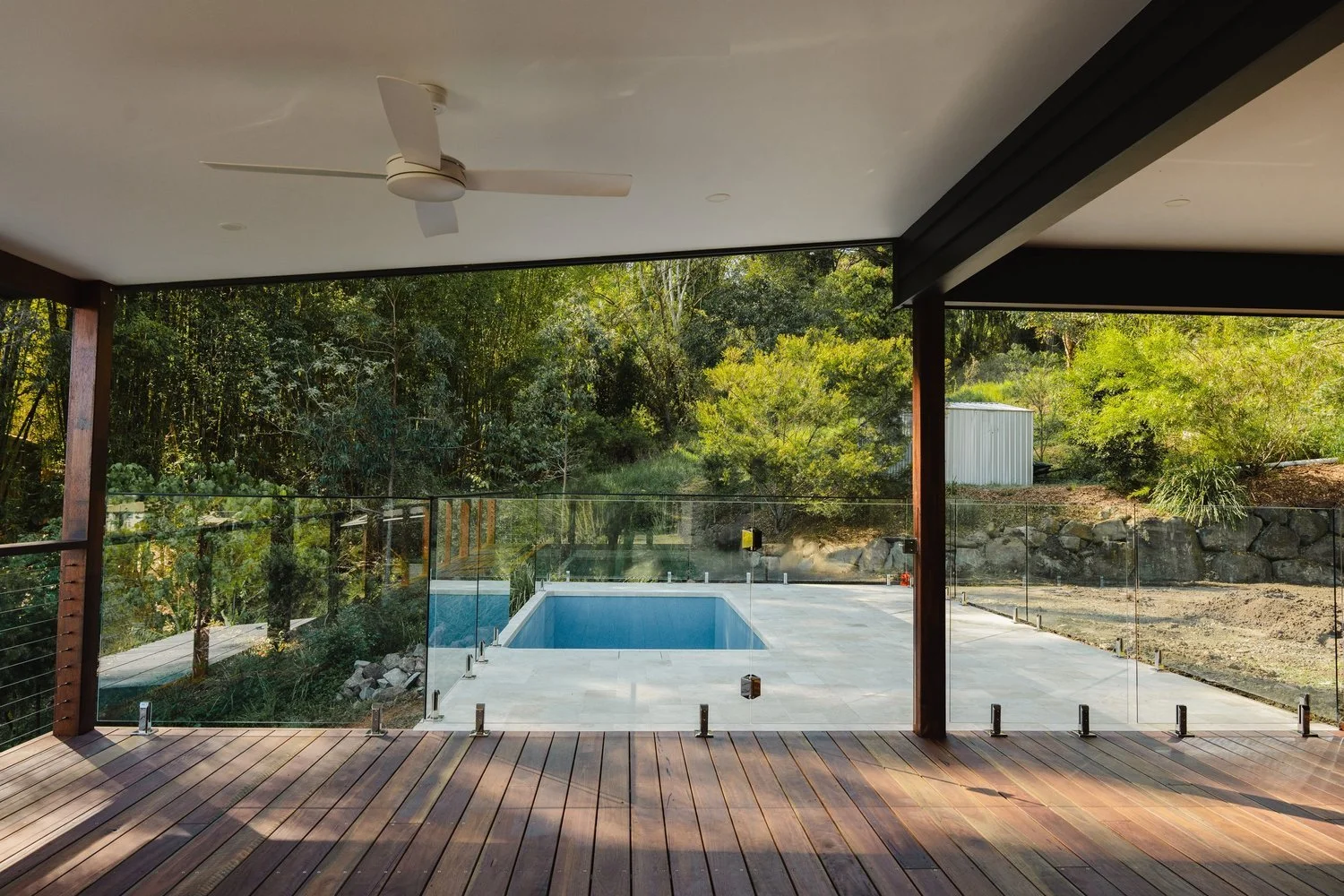 Covered patio with wooden floor overlooking a backyard with a swimming pool and trees.