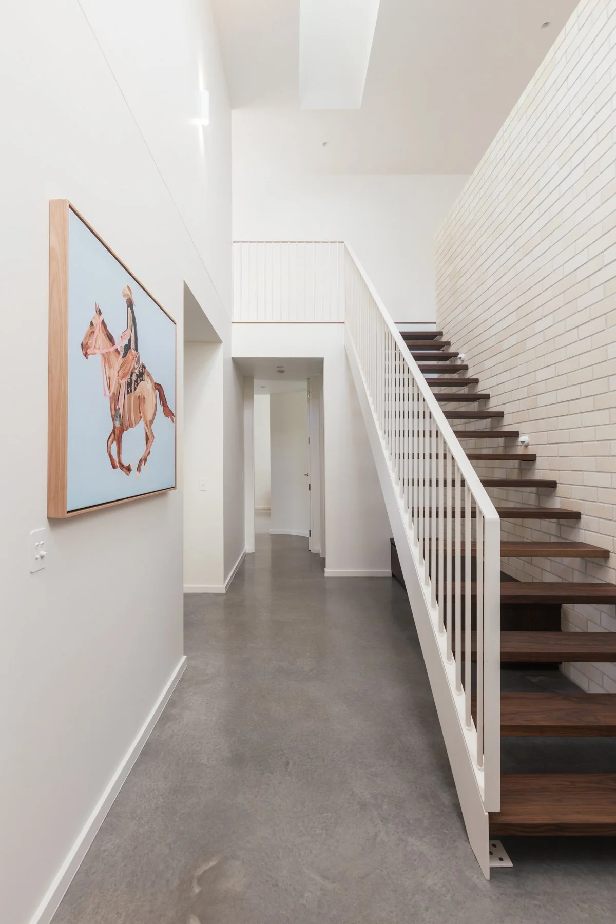 Modern interior hallway with a staircase, white walls, and artwork of a person riding a horse on the left wall.