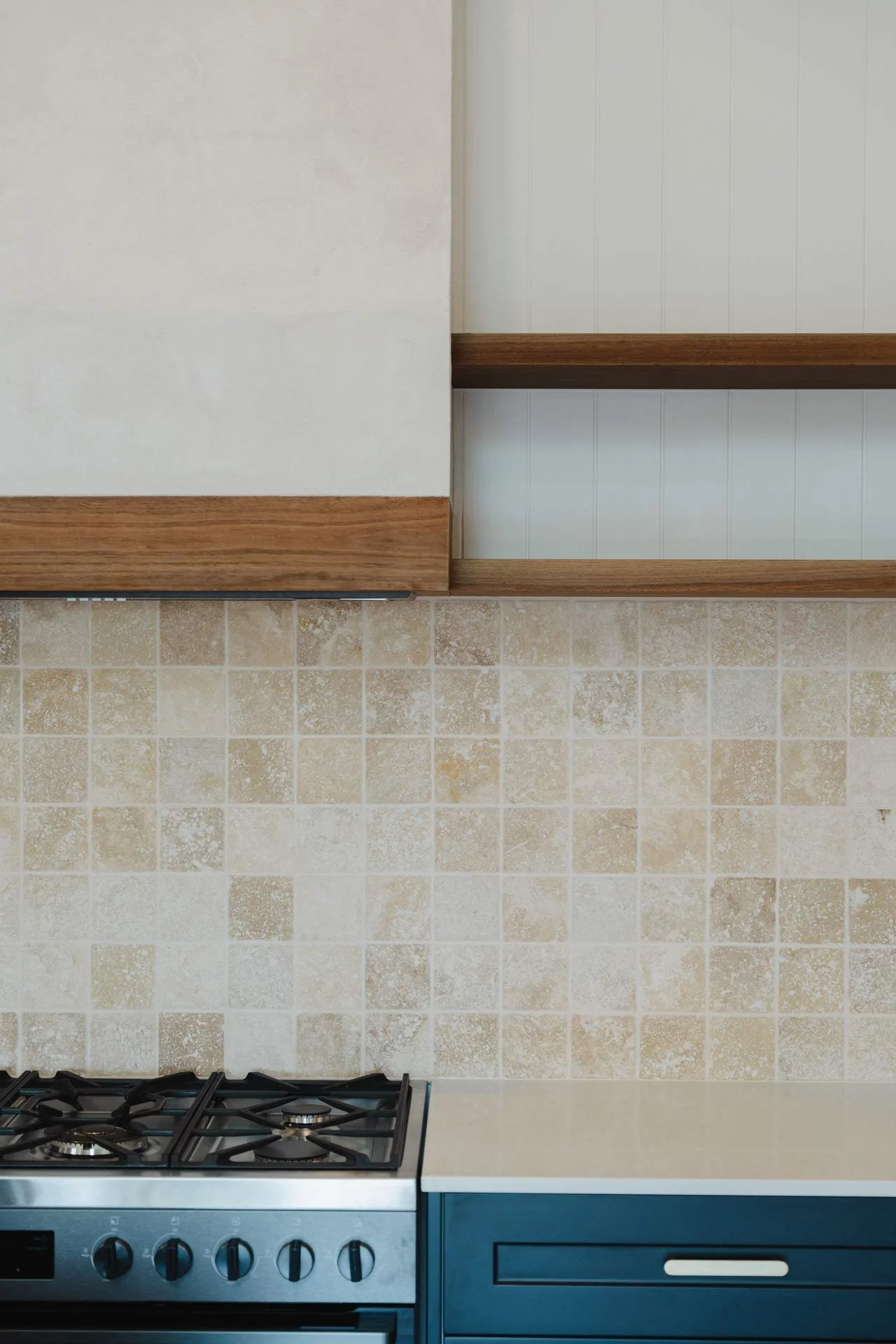 Kitchen with beige tiled backsplash, dark blue cabinets, beige countertop, and a stainless steel gas stove.