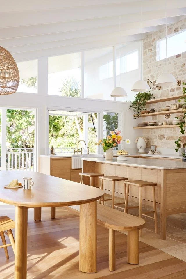 Bright, airy kitchen with wood furniture, open shelves, and large windows overlooking greenery.