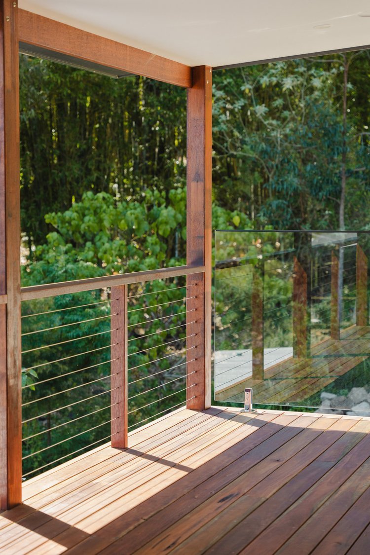 A balcony with wooden flooring and railing, overlooking lush green trees.