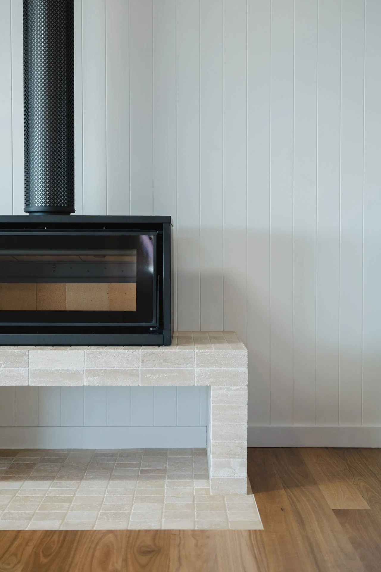 A modern fireplace with a black glass front, set on a white brick hearth, against a white paneled wall with a wood floor.