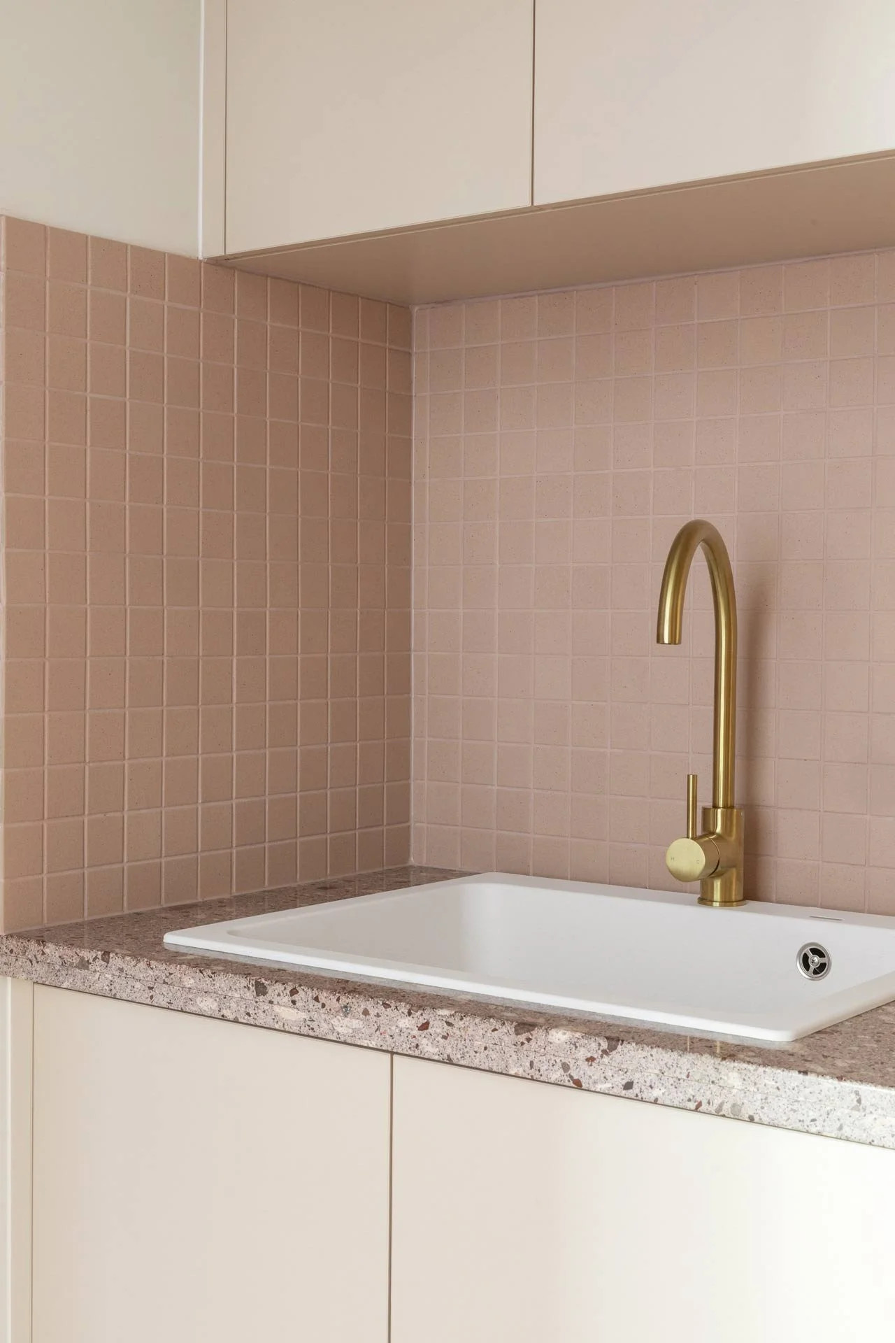 A modern kitchen sink with a gold faucet, beige tiled backsplash, and a speckled granite countertop.