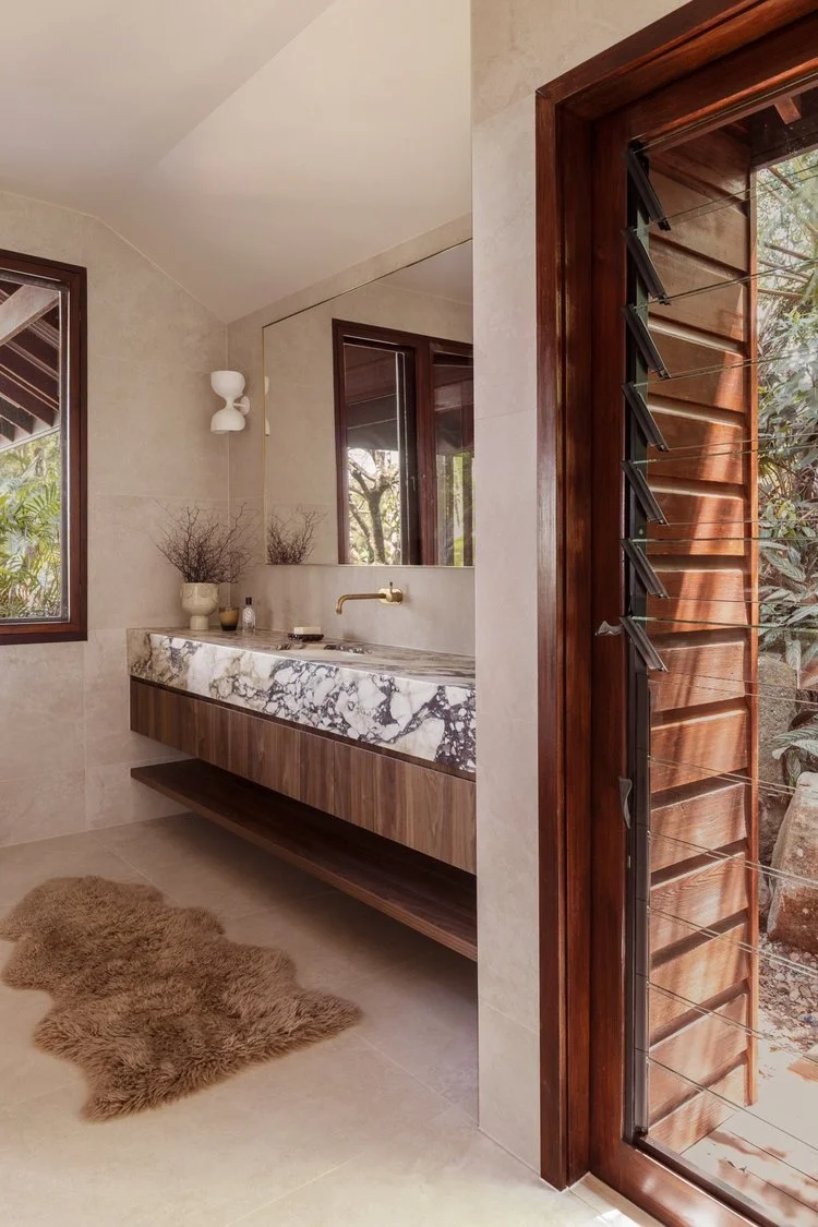 Modern bathroom with marble sink, wooden cabinet, window, and sliding wooden louvered door.