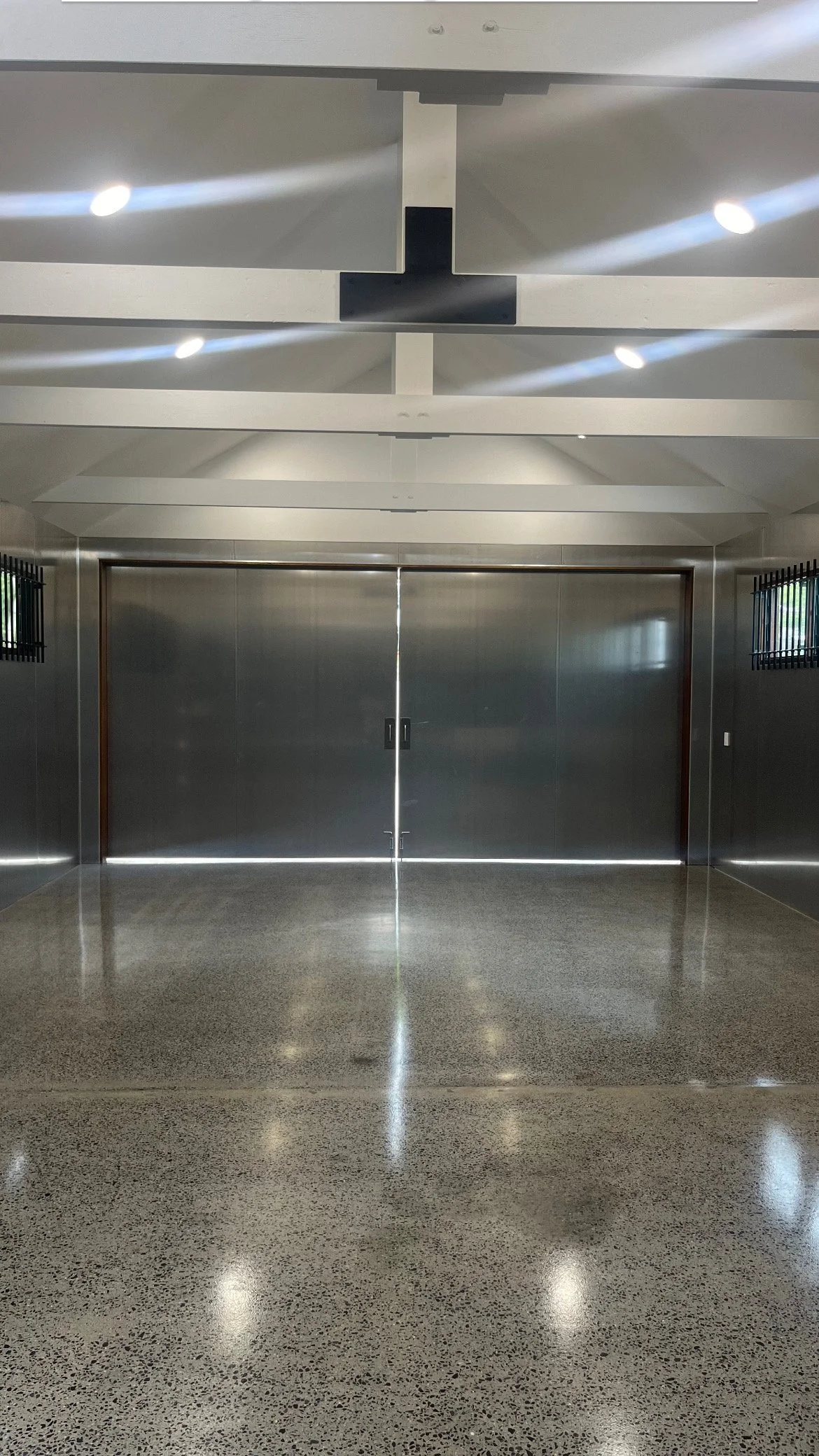 Closed gray metal doors in an indoor space, with polished speckled floor and minimal lighting.
