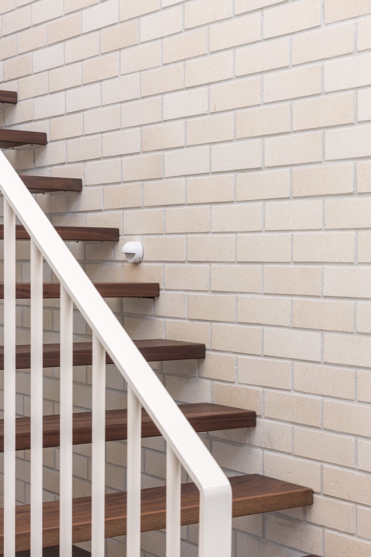A staircase with wooden steps and white railing against a beige brick wall.