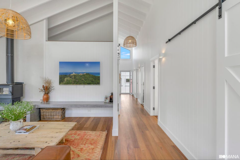 Bright, modern hallway with white paneling, hardwood floors, and a wall-mounted TV showing a landscape with hills and a lighthouse.