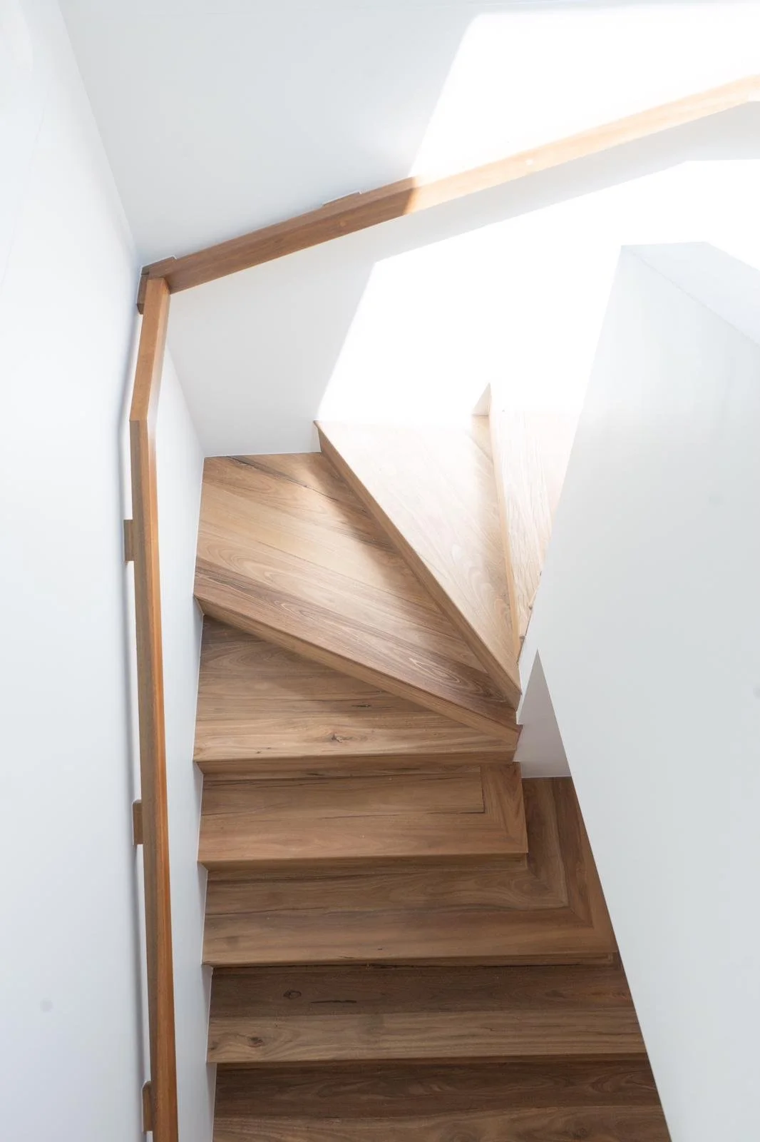 A wooden staircase viewed from above, with white walls and natural light coming from above.