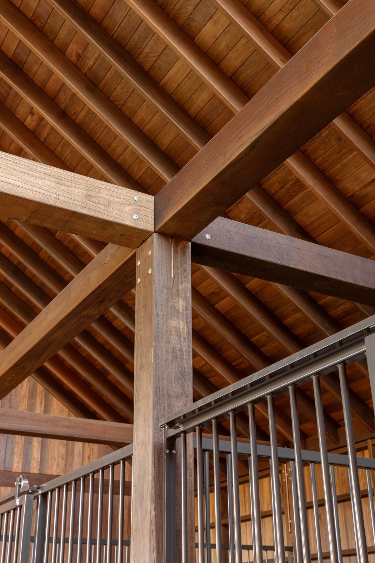Interior of a wooden and metal structure, possibly a barn or stable, with a wooden ceiling and wooden beams supporting a balcony or upper level with metal bars.