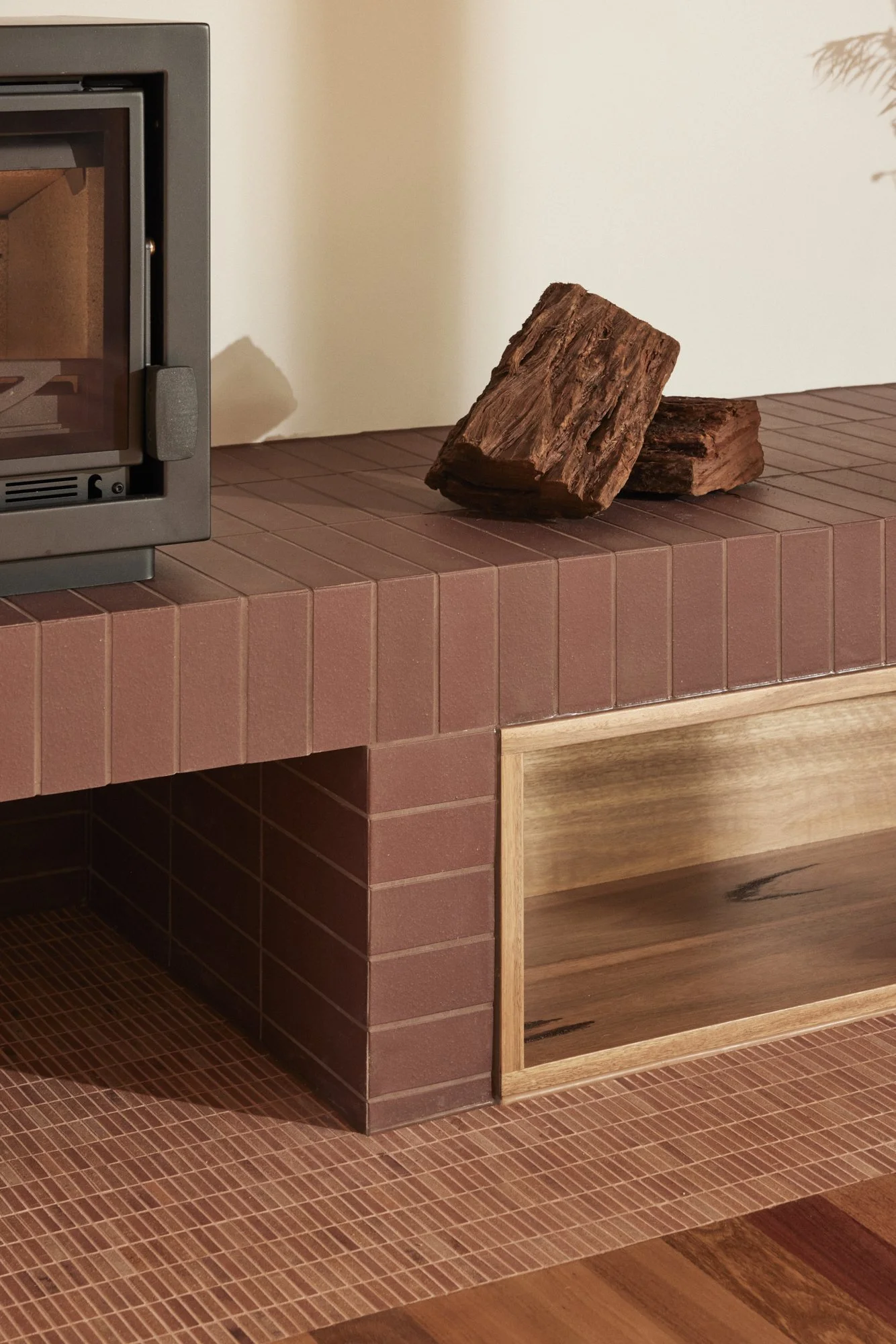 A corner of a room with a wood stove on a tiled hearth, and two pieces of firewood resting on top of the tiles.
