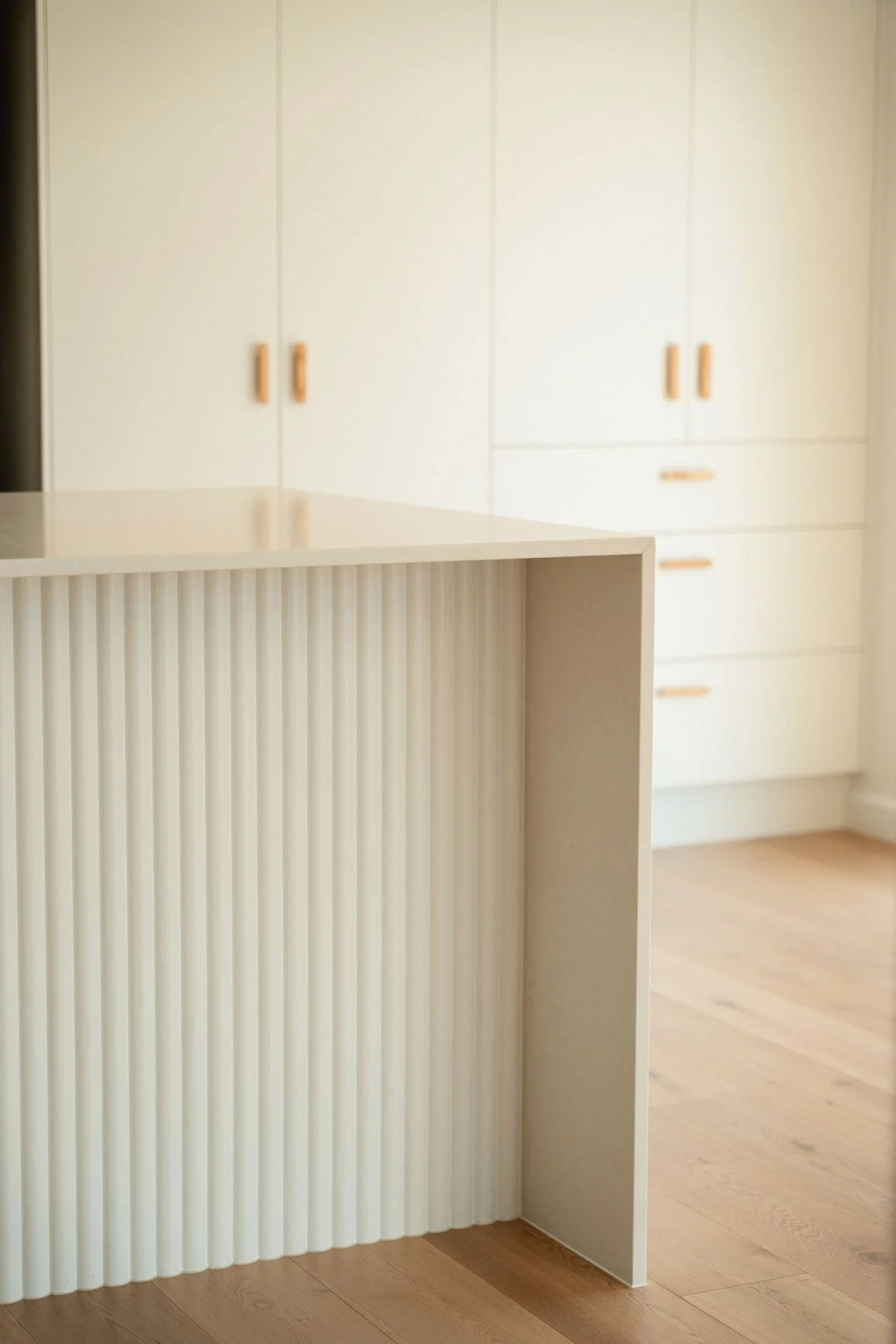 A modern white kitchen with cabinets, a partial view of a wooden counter or island, and light wood flooring.