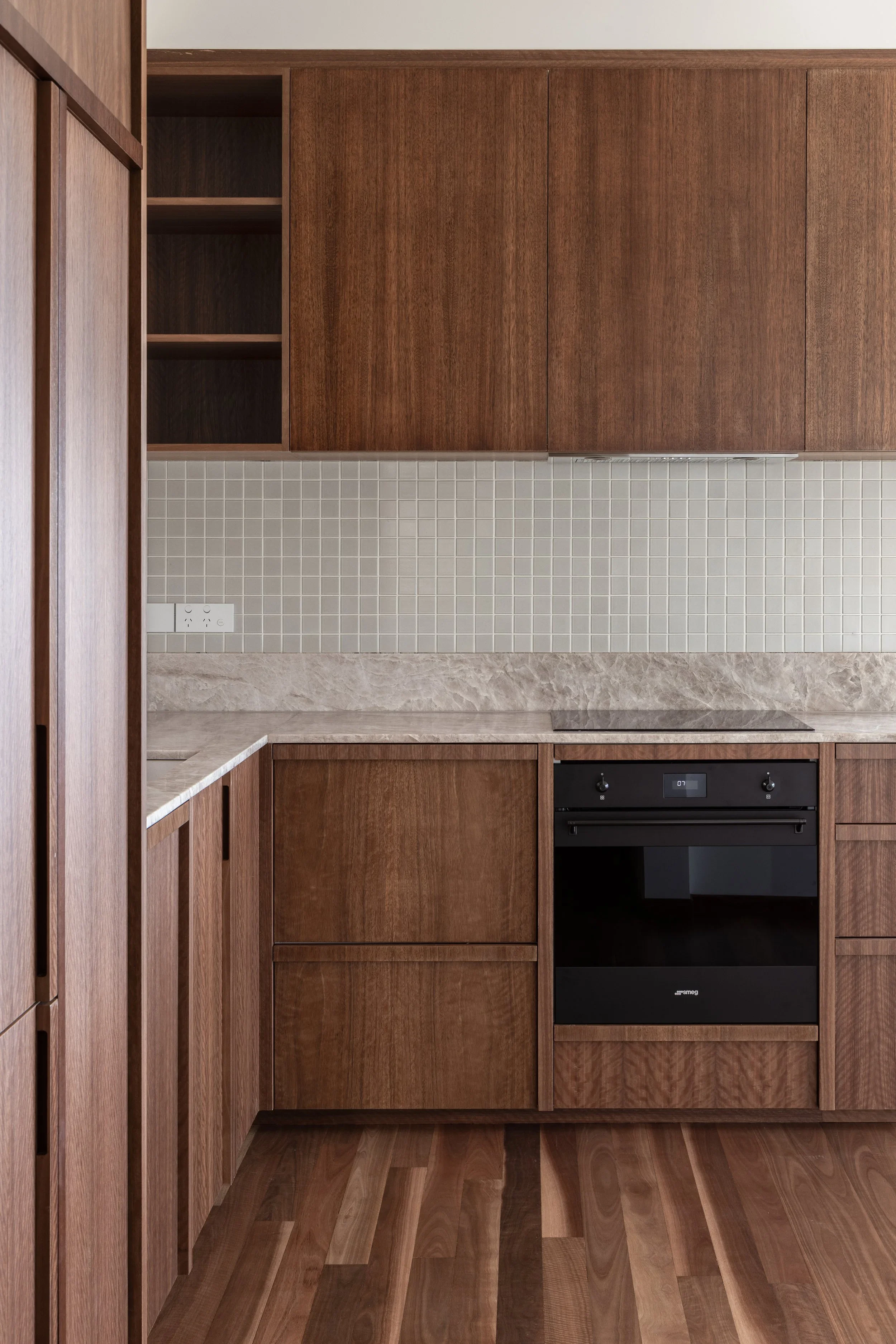 A modern kitchen with wooden cabinets, a black oven, a gray backsplash, and a light-colored marble countertop.