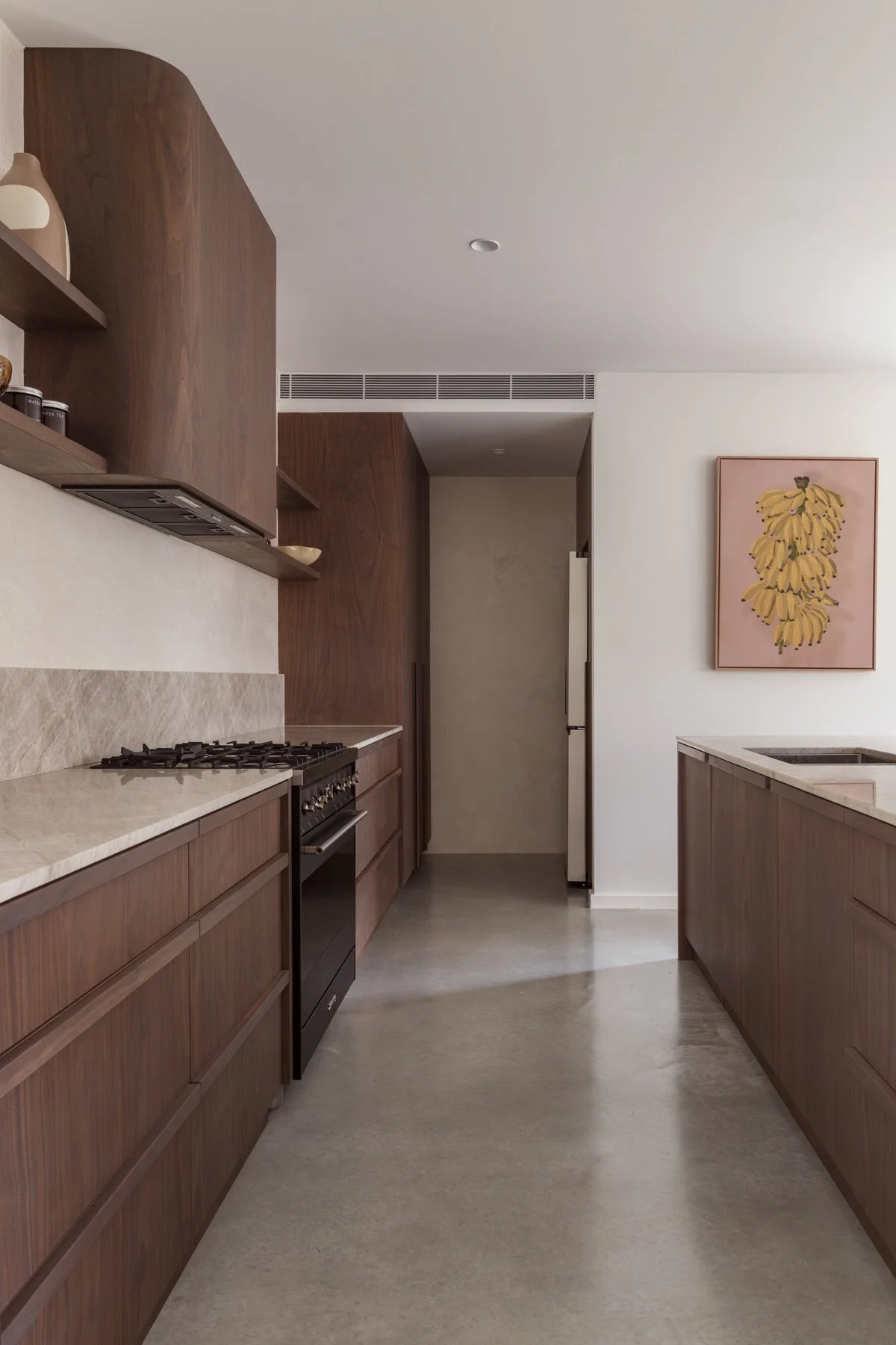 Modern kitchen with wooden cabinets, beige marble countertops, a built-in gas stove, minimalist decor, a framed artwork of bananas on the wall, and a white ceiling with recessed lighting.