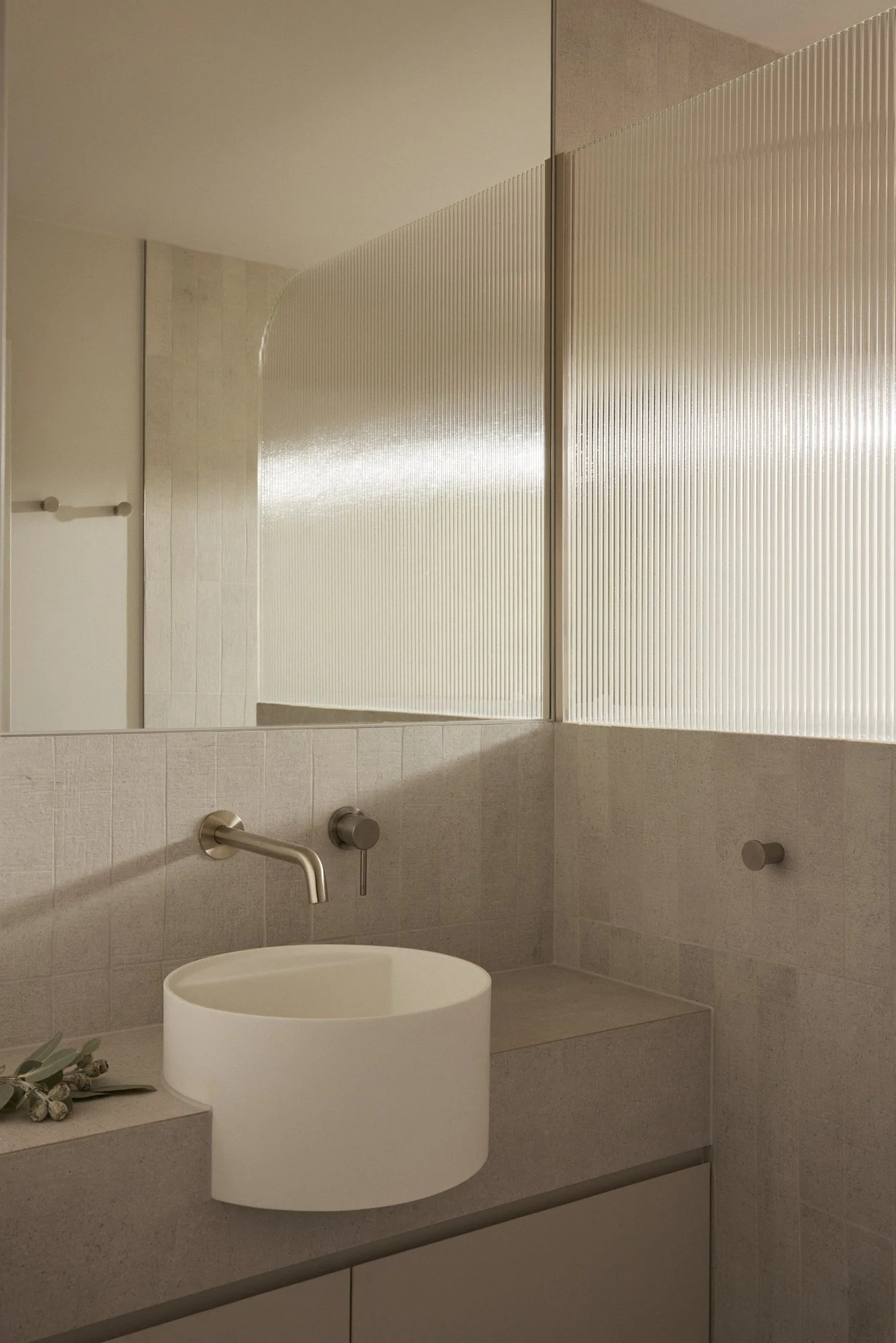 Modern bathroom with a round white vessel sink, wall-mounted faucet, beige tiled walls, frosted glass partition, and a mirror above the sink.