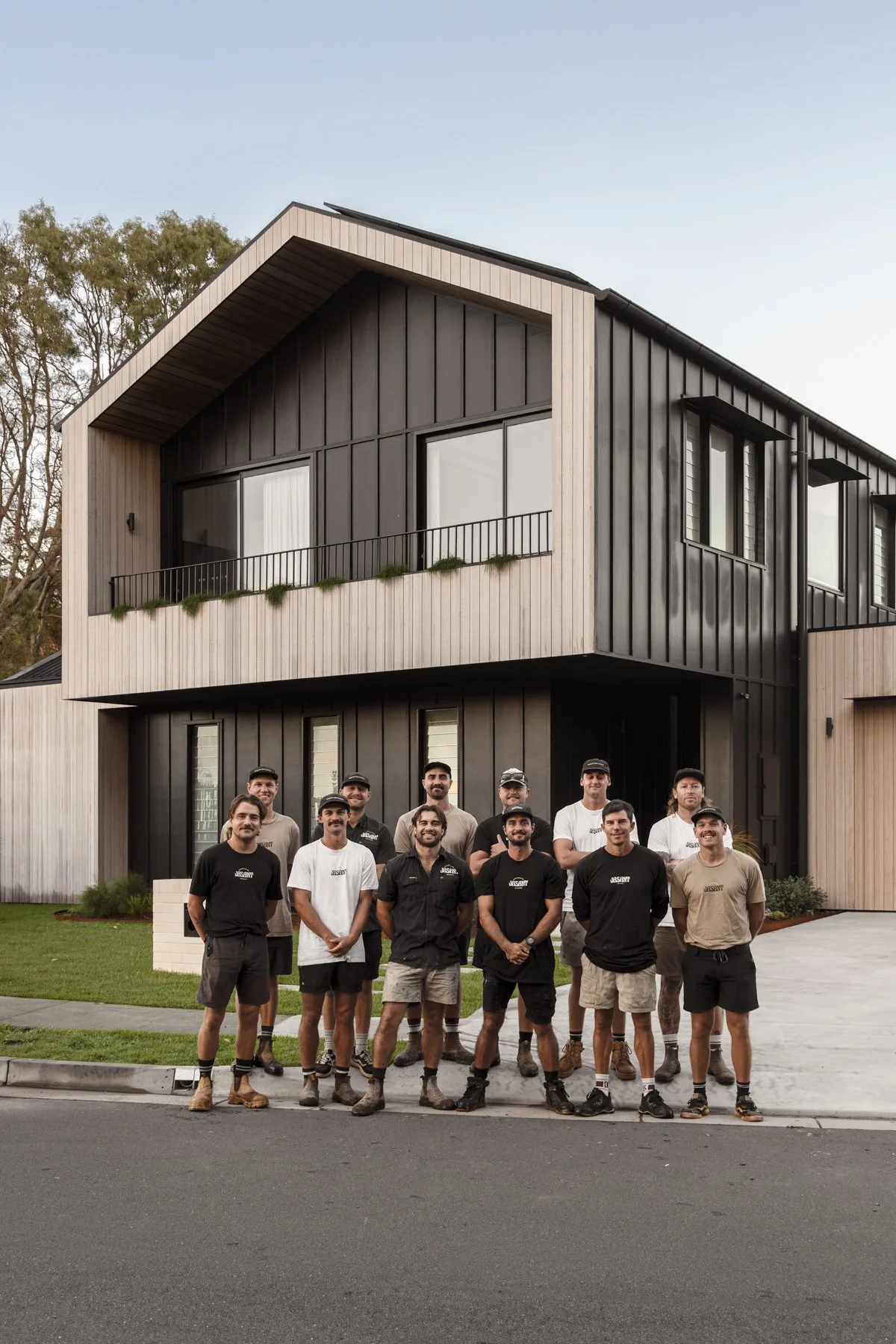 Group of men standing in front of a modern two-story house with a black and wooden exterior.