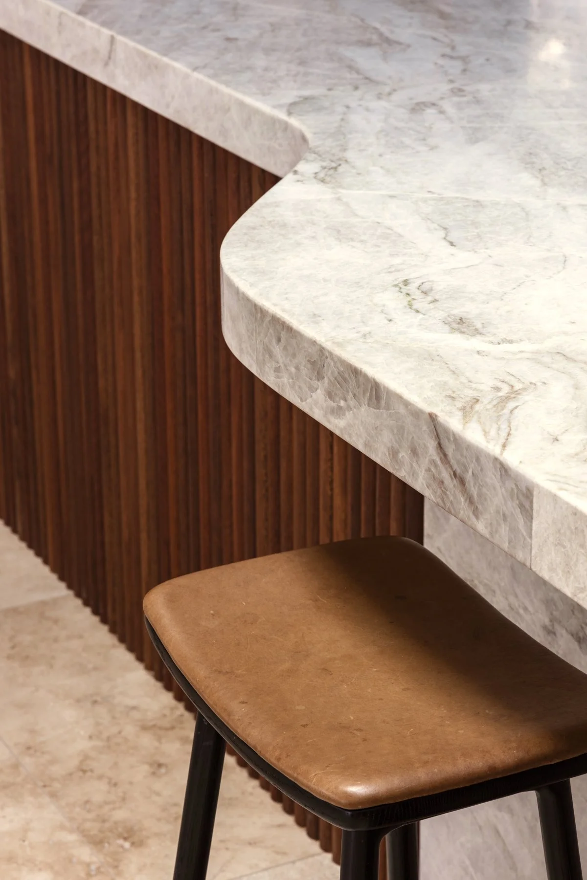 Close-up of a barstool with a brown leather seat in front of a marble countertop with a wood-paneled side.