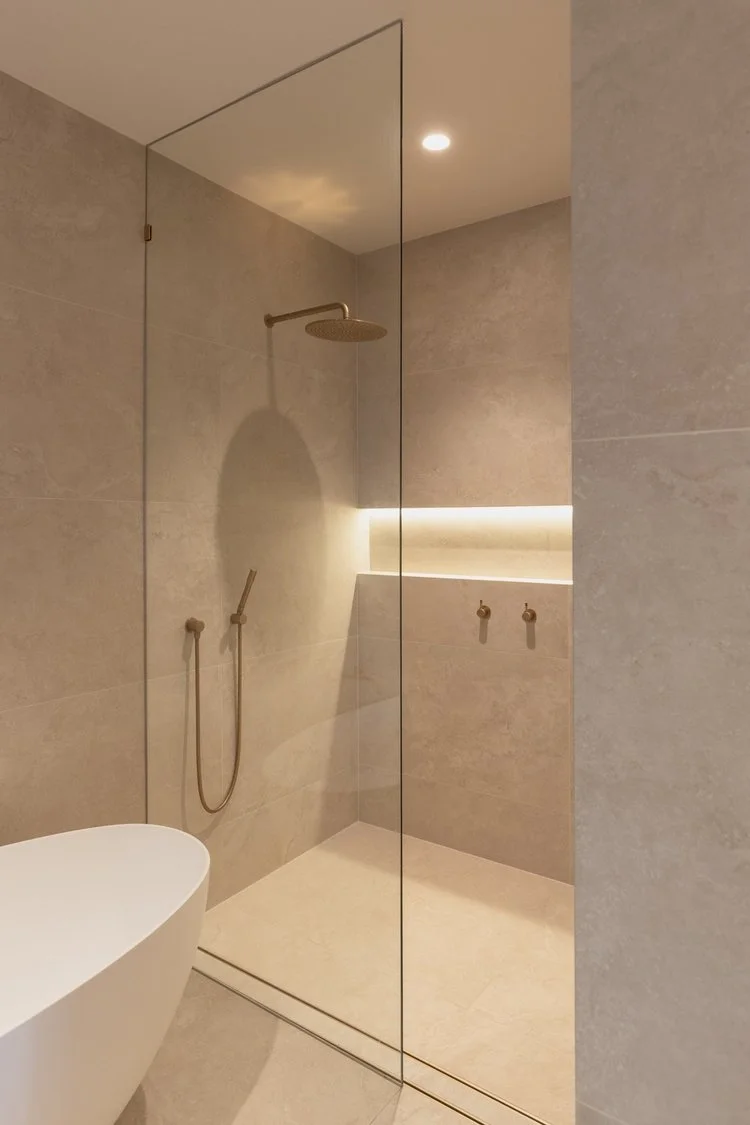 Modern walk-in shower with beige tiles, a rain showerhead, a handheld shower, and built-in lighting, separated by a glass panel.