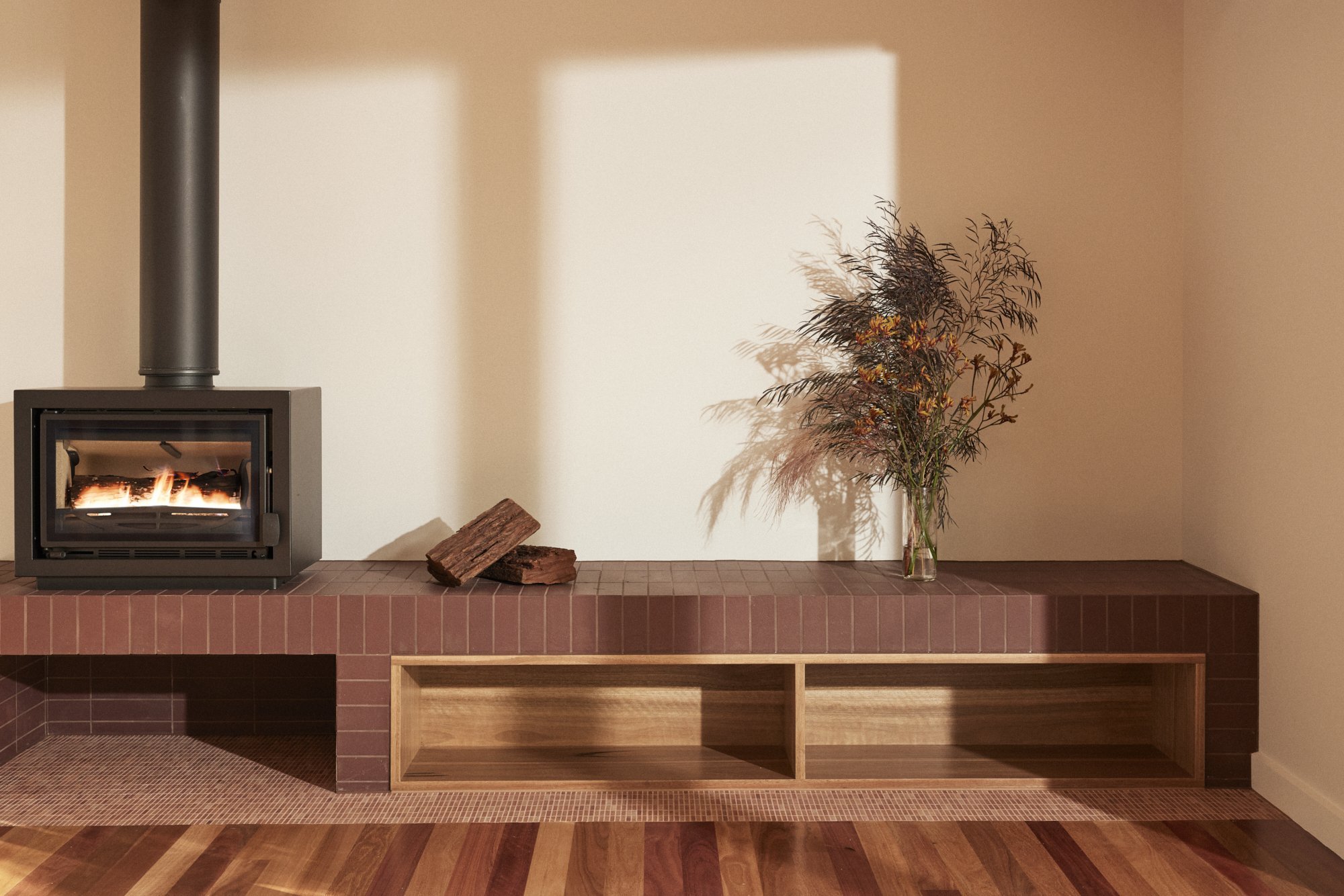 A modern fireplace with wood logs, a vase of dried plants, and a brick mantel in a minimalist room.