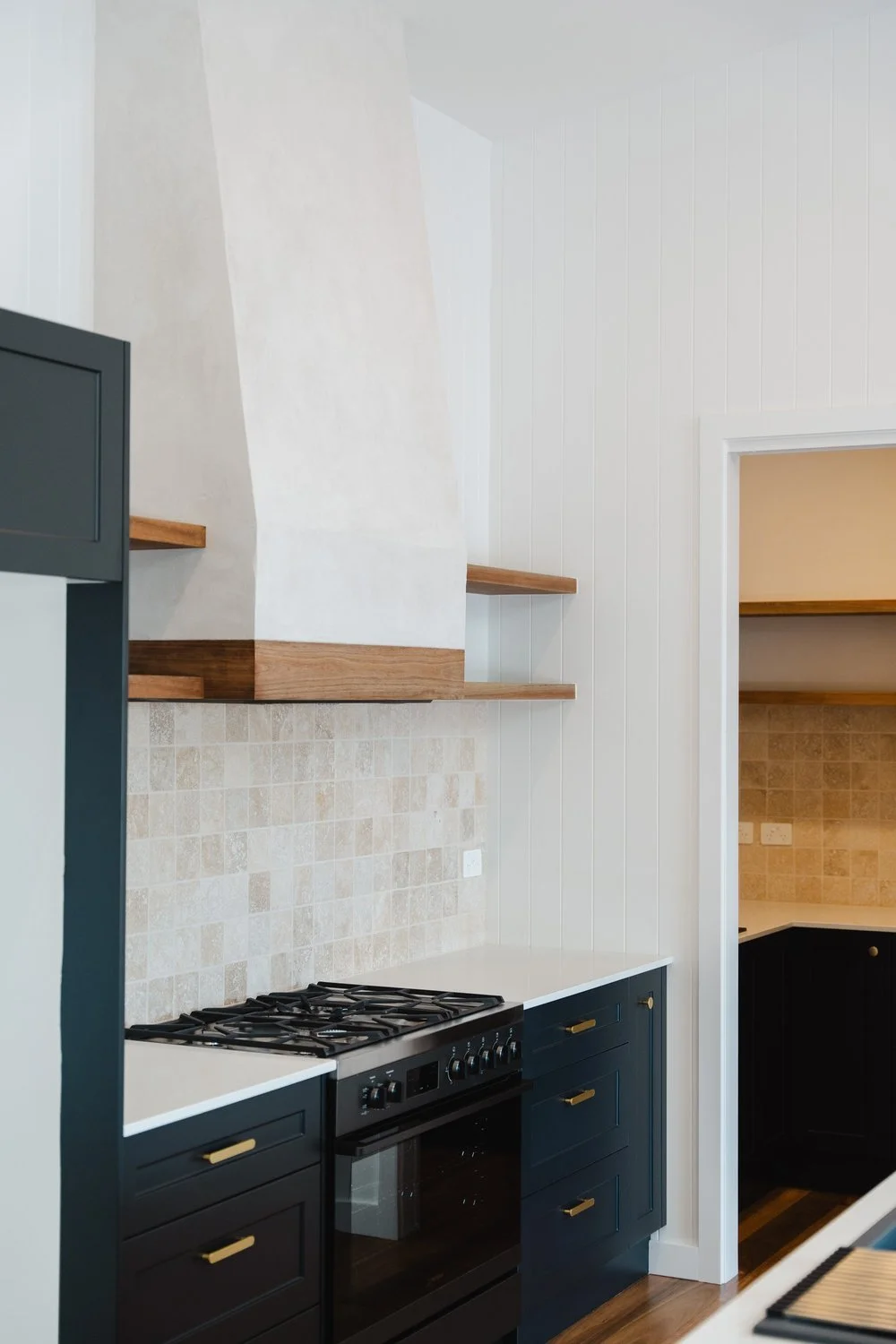 Modern kitchen with black cabinets, gold handles, beige backsplash, and open wooden shelves.