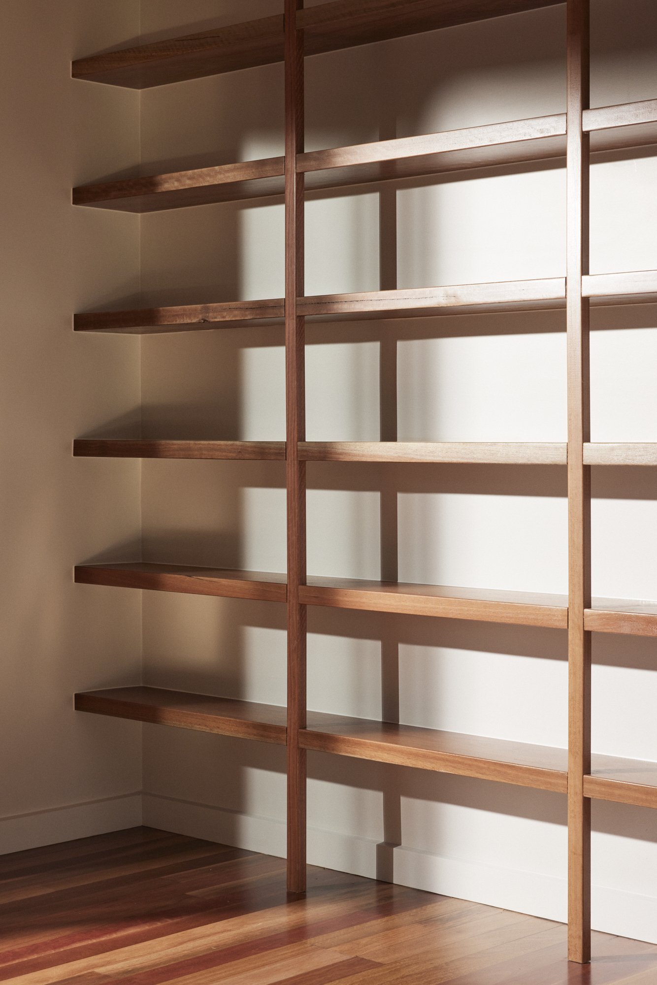 Wooden bookshelf with multiple empty shelves next to a wall with shadows cast on the wall.