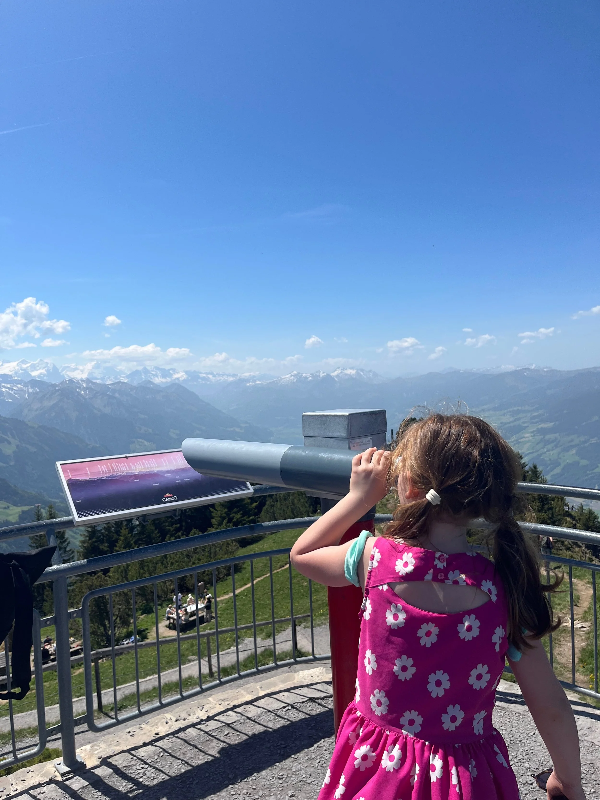 Child looking through a viewfinder telescope at an Alpine mountain panorama — Small Steps Explorers
