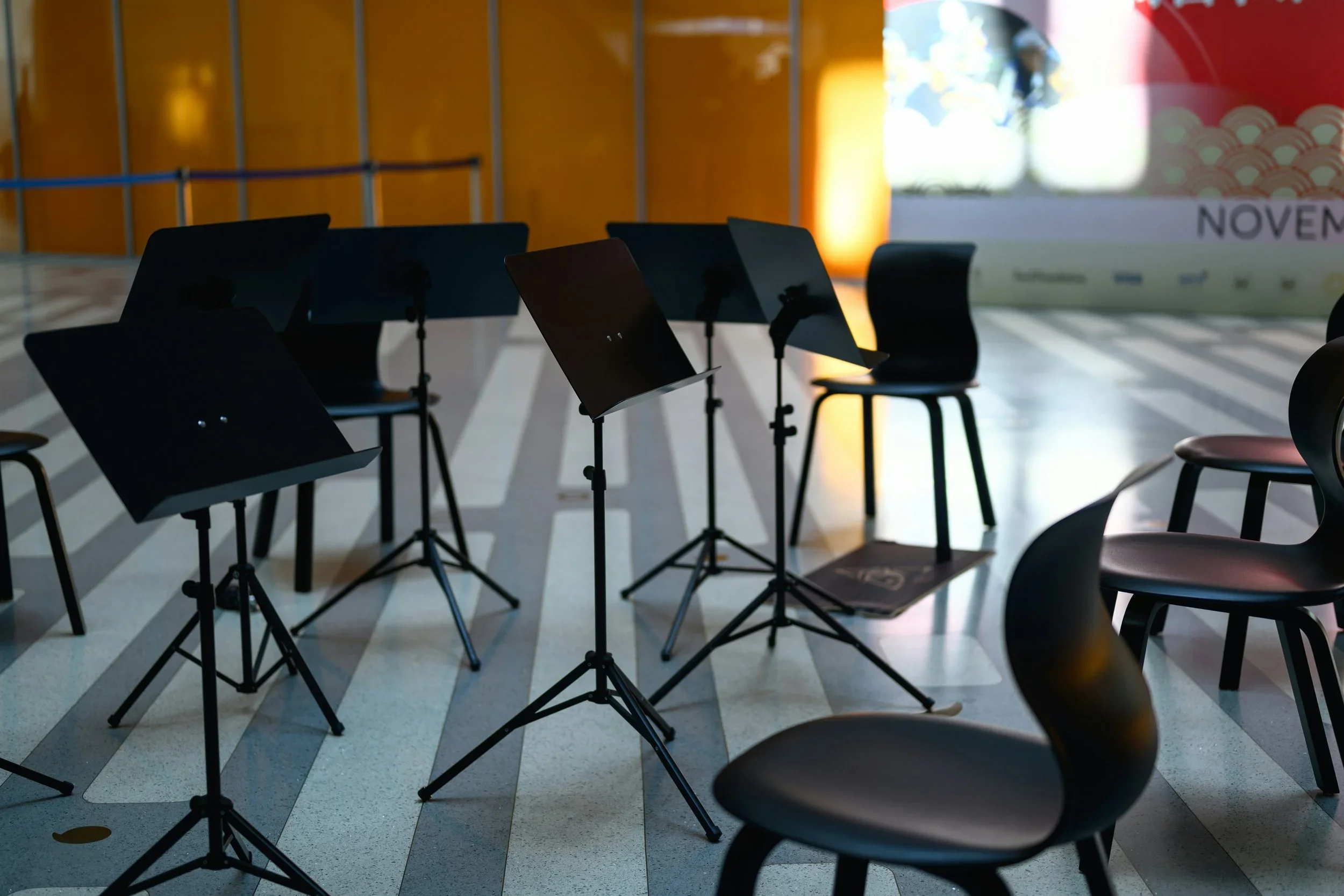 Chaises vides et partitions de musique sur des pupitres dans une salle de concert ou de répétition, avec un éclairage tamisé.