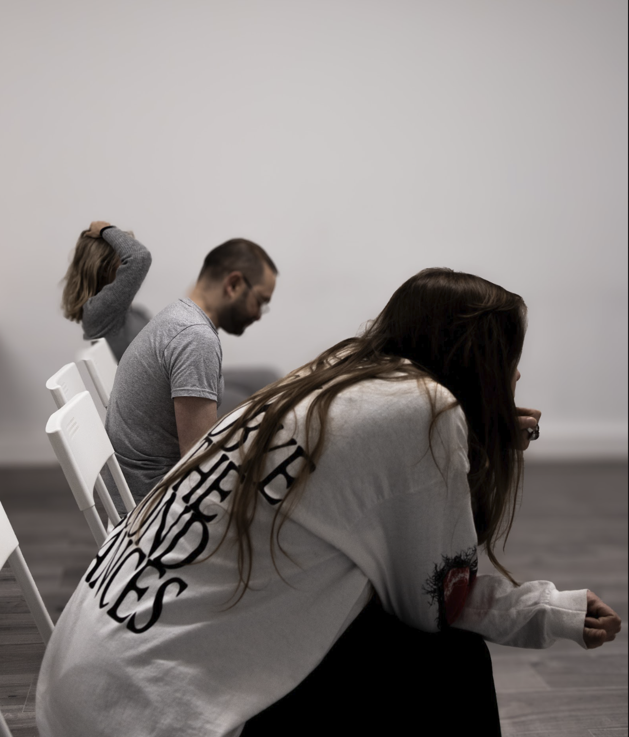 Three people sitting in a row of chairs with heads bowed and eyes closed, appearing to be in prayer or meditation.