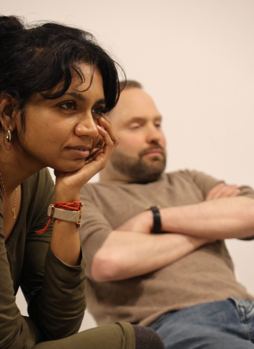 Two people sitting closely, appearing attentive and thoughtful in a neutral-colored room.