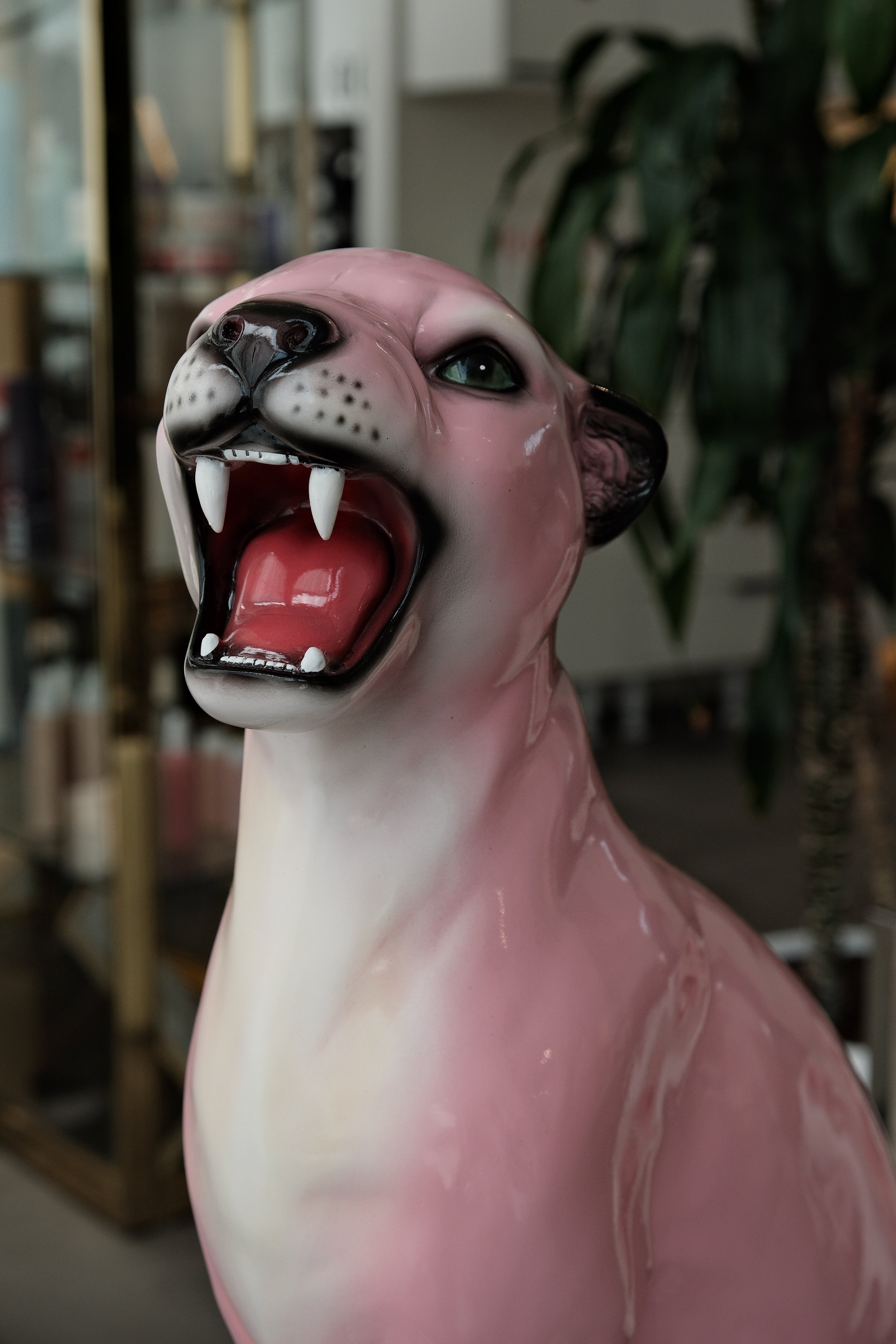 Close-up of a pink saber-toothed cat statue with green eyes and an open mouth