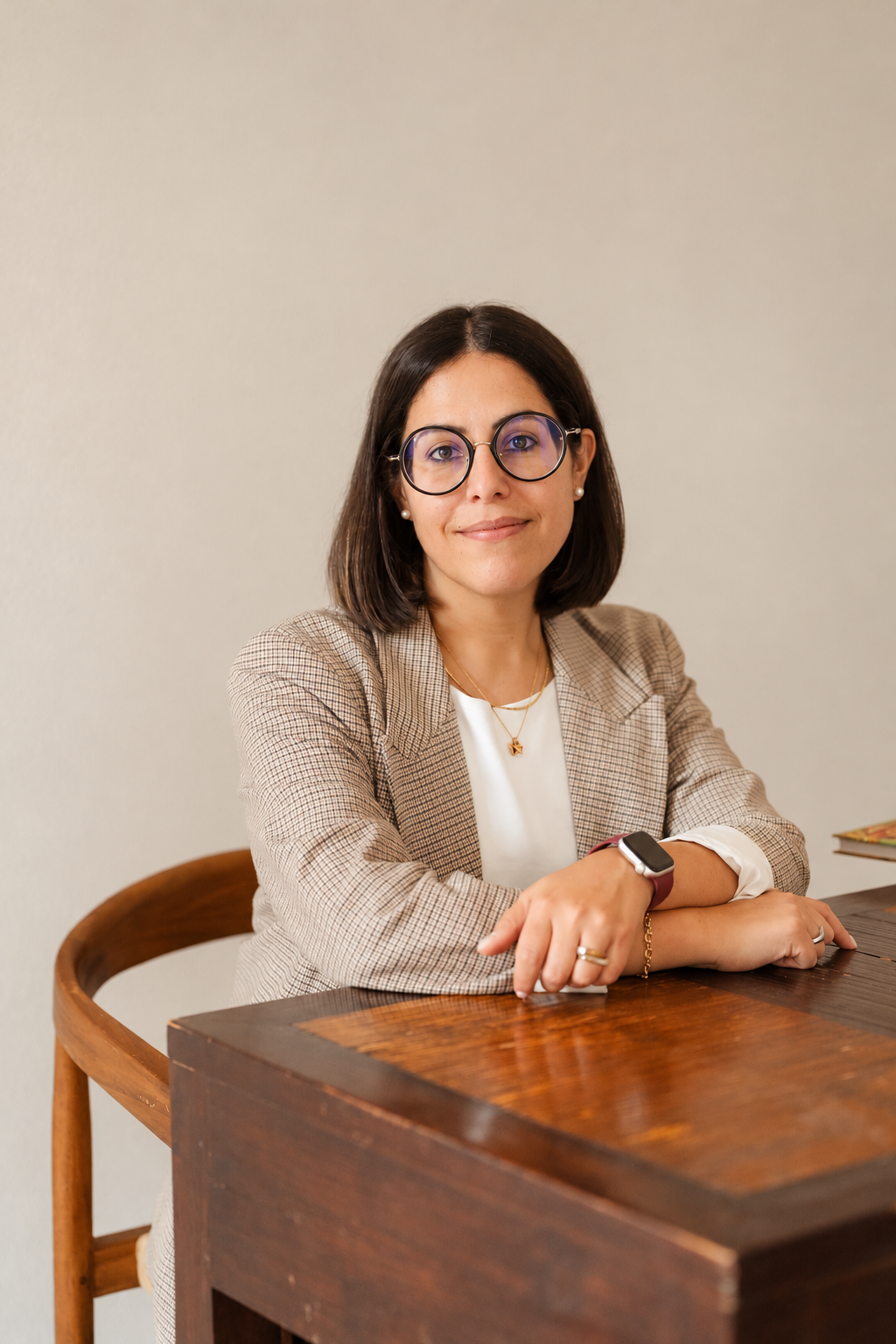 Dottoressa chirurgo valeria quintodei nutrizionista seduta a un banco di legno in abiti professionali, con occhiali tondi, capelli castani corti e un sorriso, in un ambiente neutro.