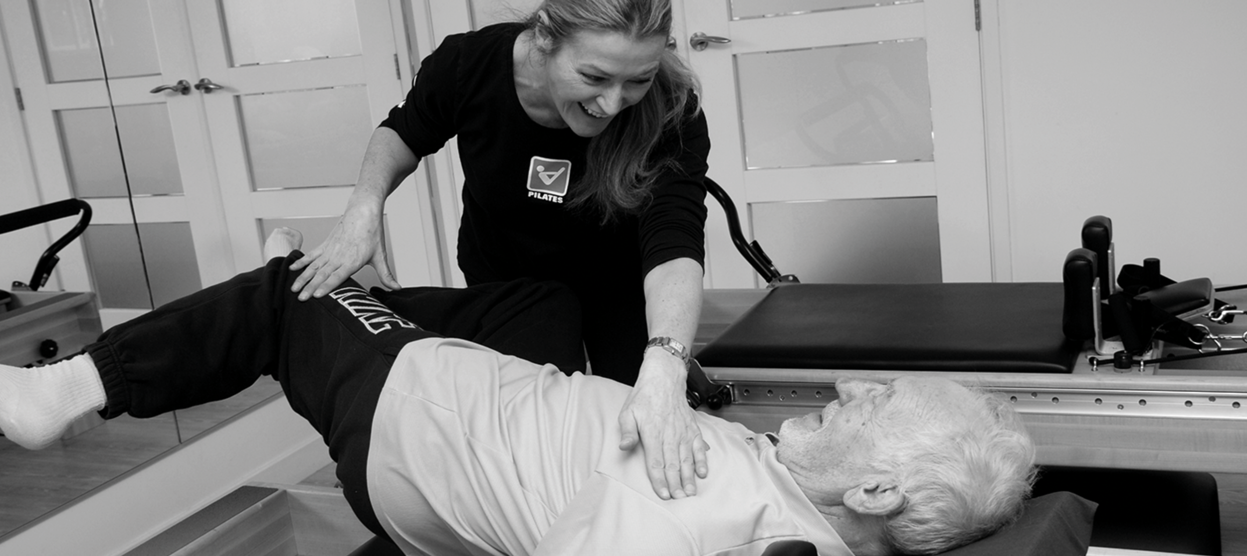 A woman performing CPR on an elderly person lying on a medical examination table.