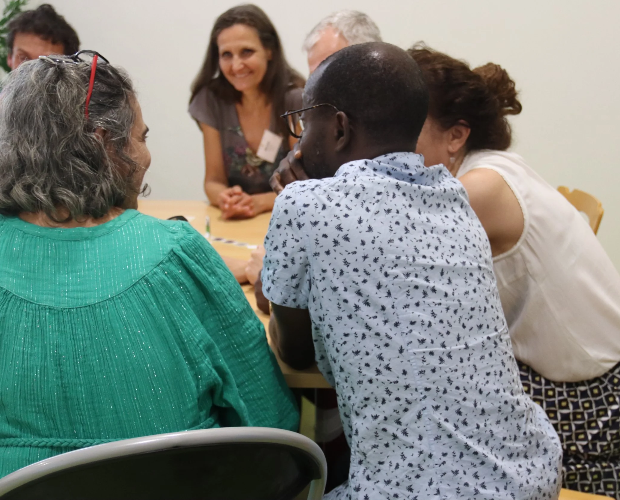 Group of diverse people sitting around a table engaged in a discussion, with one woman smiling and facing the others.