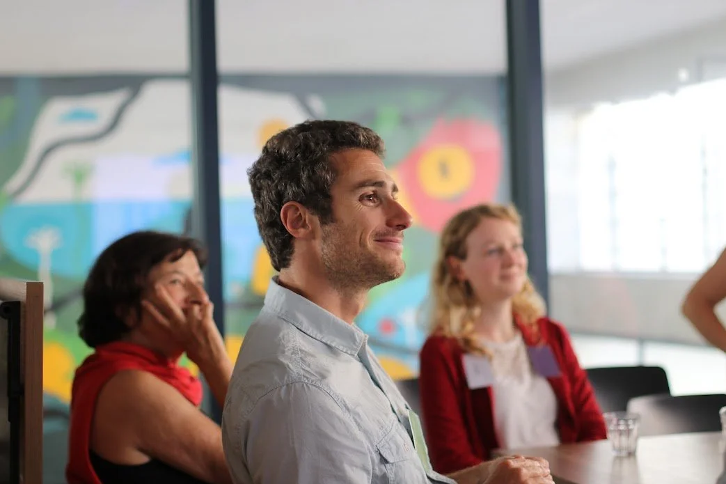 People sitting at a table and interacting in a team coaching, with a colorful mural in the background.