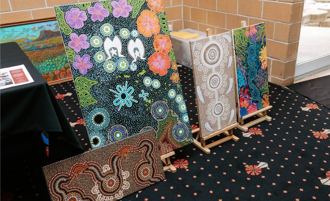 A display of five Aboriginal dot-painted artworks on small easels on a table with a black tablecloth, featuring colorful and patterned designs.