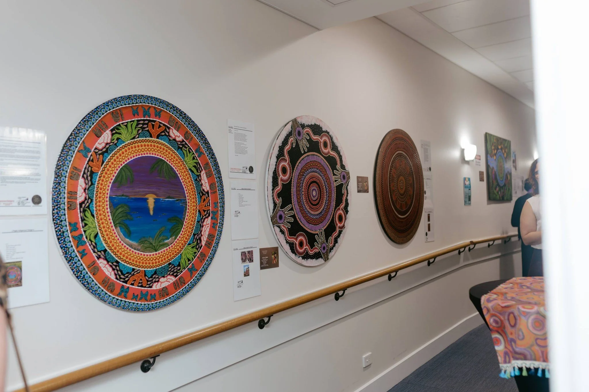 Art gallery wall featuring three circular paintings with intricate patterns and bright colors, and informational plaques beside each artwork.