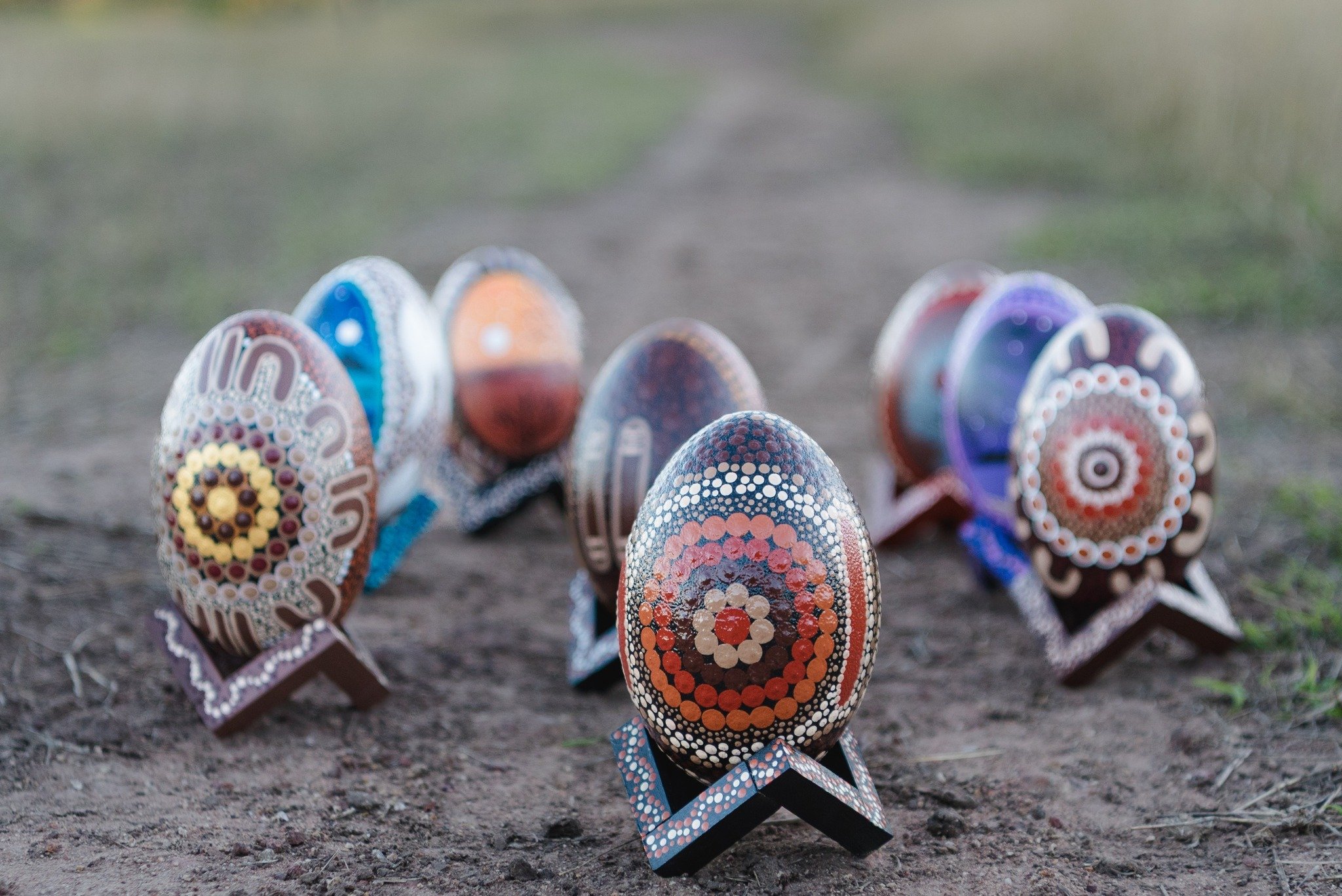 Colorfully decorated eggs with intricate dot patterns, arranged on the ground outdoors.