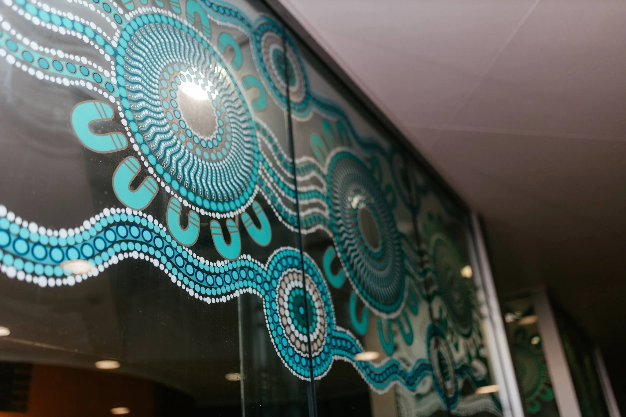 Close-up of an intricate, circular dot painting with shades of blue, white, gray, and black, reflecting on a glossy surface, possibly a painted wall or mural.