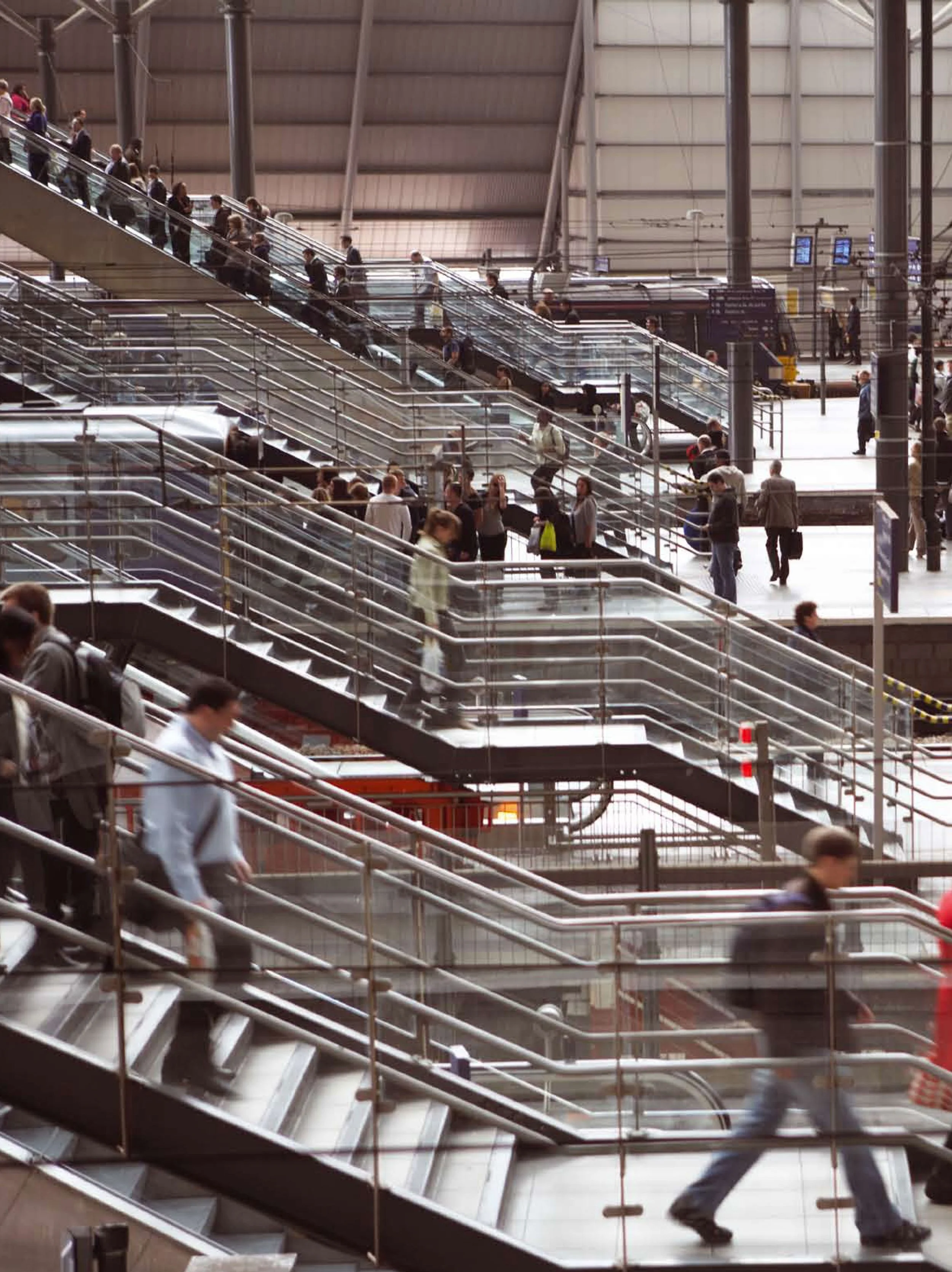 People riding escalators and walking through a busy train station or airport terminal.