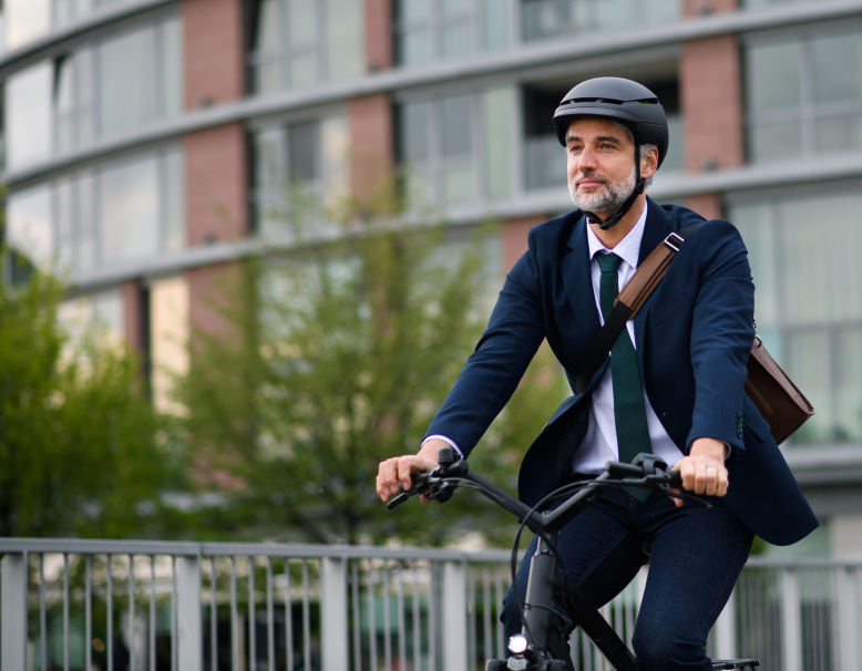 A man wearing a business suit and helmet riding a bicycle outdoors in an urban area.