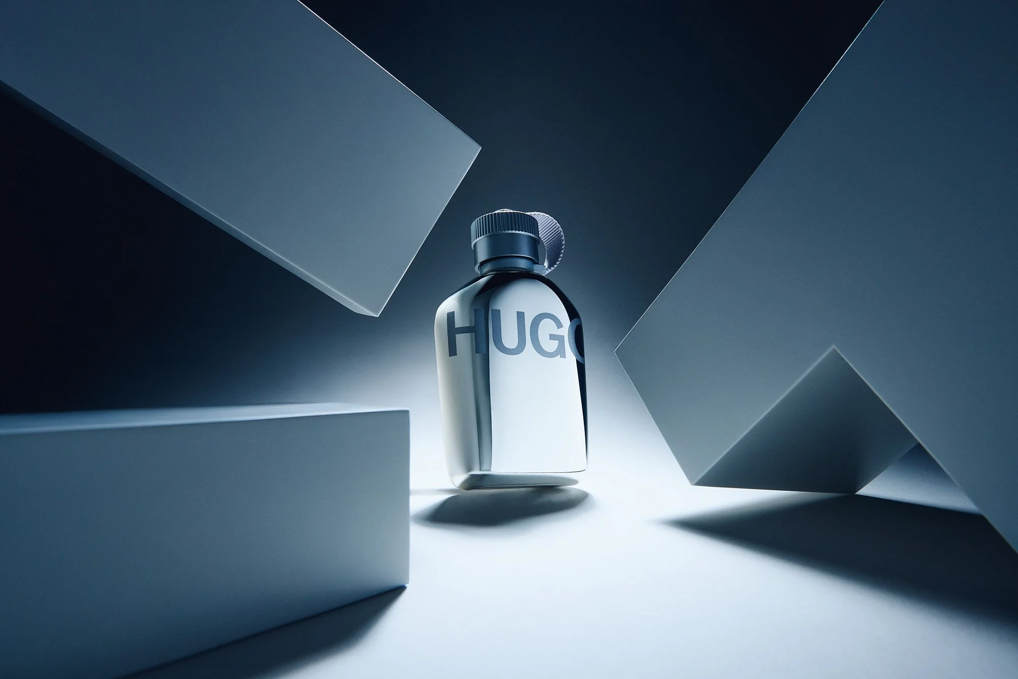A white perfume bottle labeled HUGO surrounded by geometric white and gray blocks in a minimalist setting.