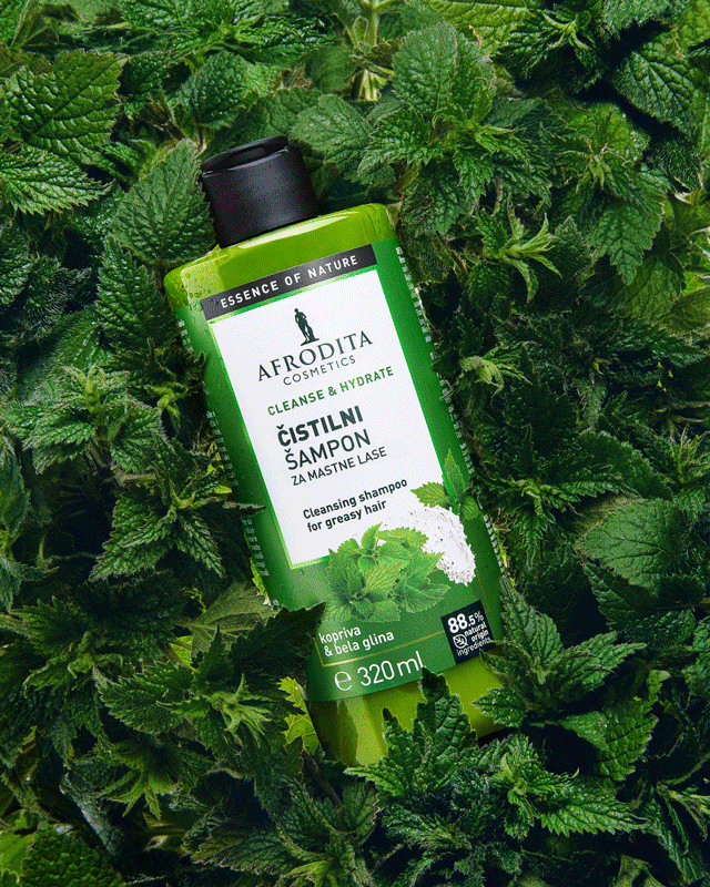 A green bottle of Afrodita Cosmetics cleansing shampoo is placed among lush green mint leaves.