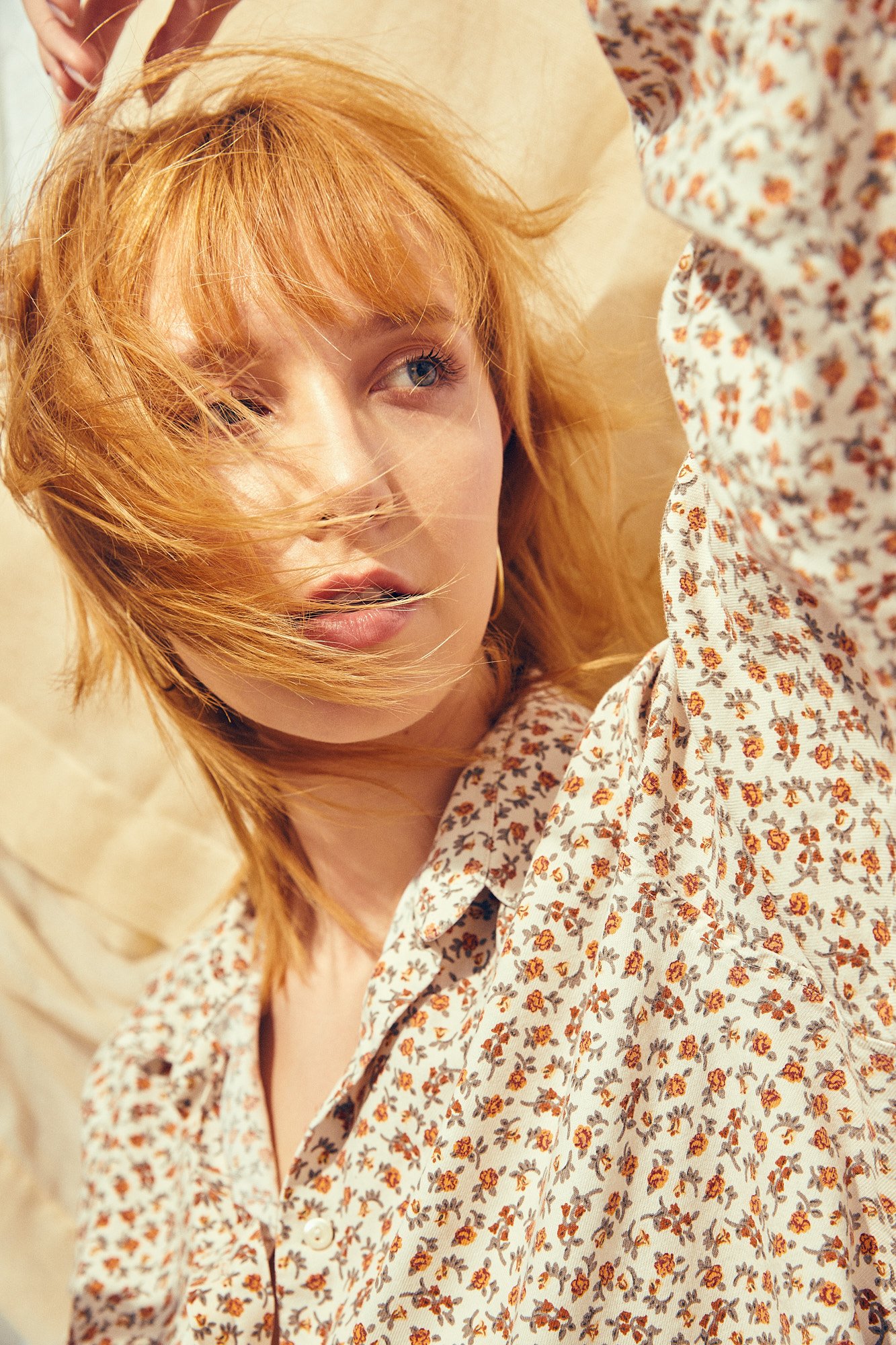 Close-up of a woman with wavy red hair and blue eyes wearing a floral shirt with orange and brown flowers.