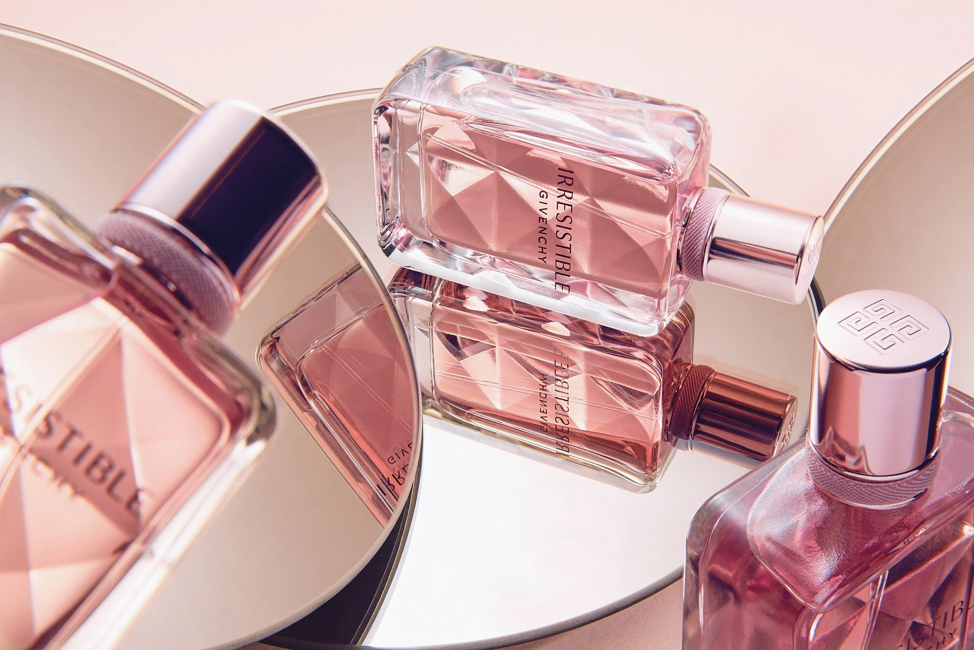 Arrangement of pink bottles of Givenchy perfume on a mirrored surface with a circular mirror in the background.