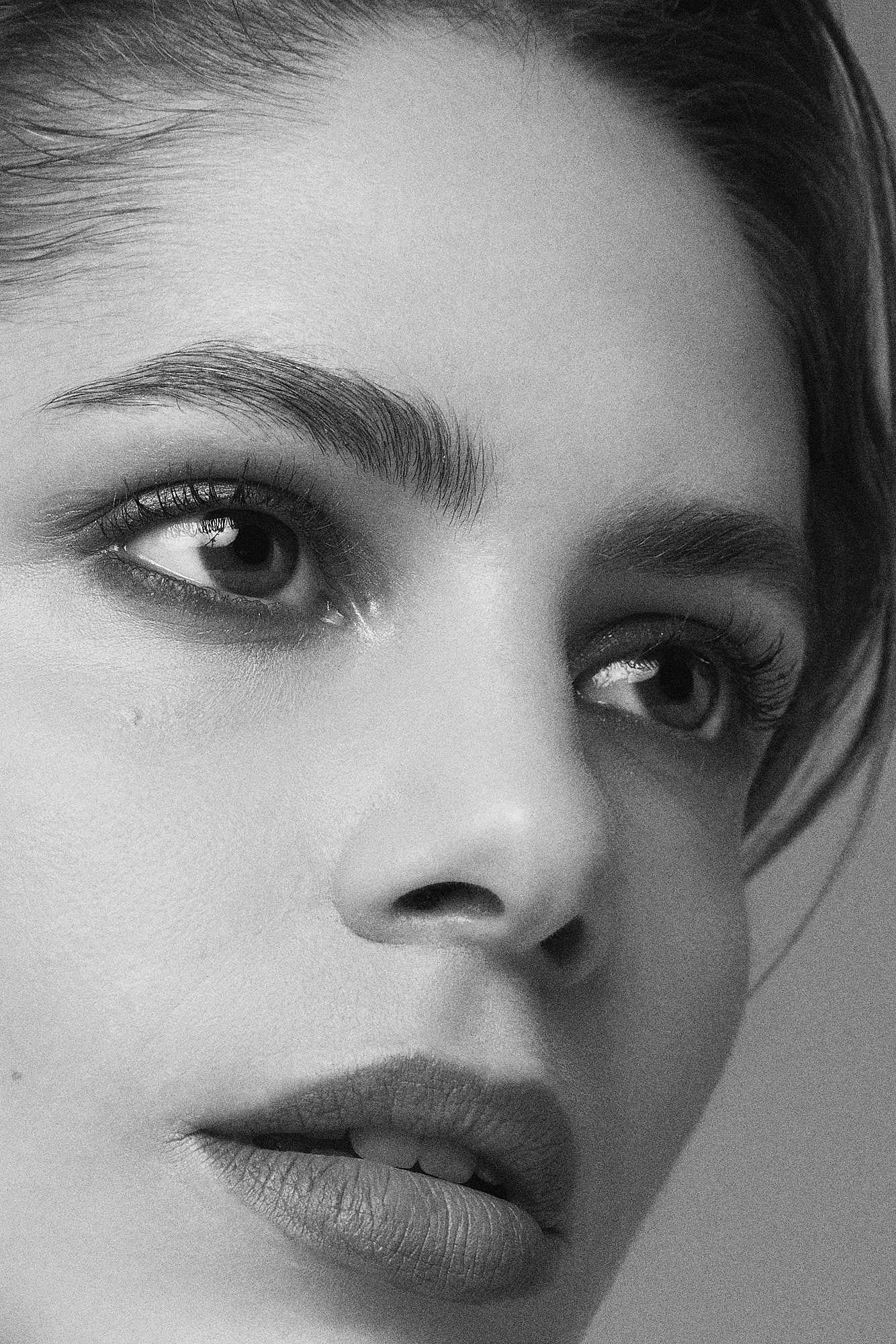 Close-up black and white photo of a woman's face showing her eye, eyebrow, nose, and lips with detailed textures and soft lighting.