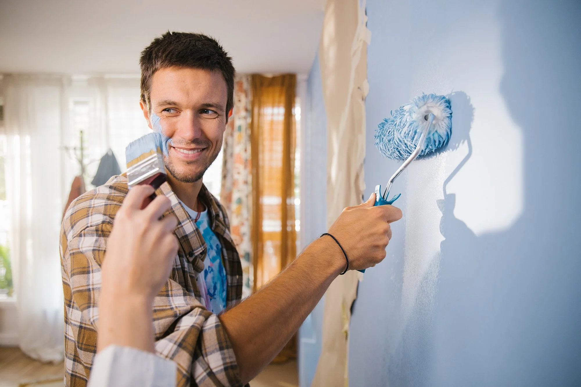 A man painting a wall light blue using a roller brush.