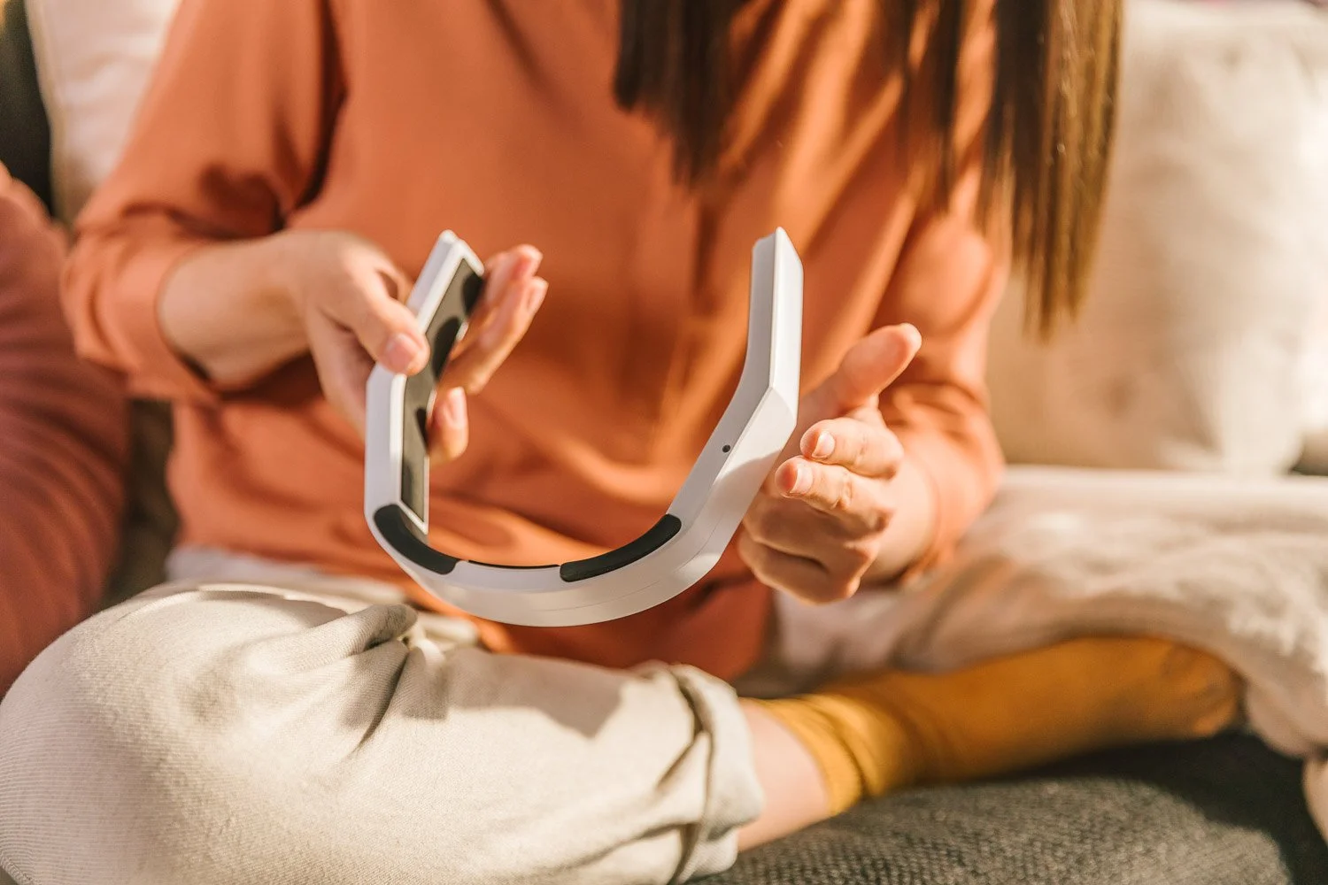 A person sitting on a sofa holding a smartphone and a white virtual reality headset.