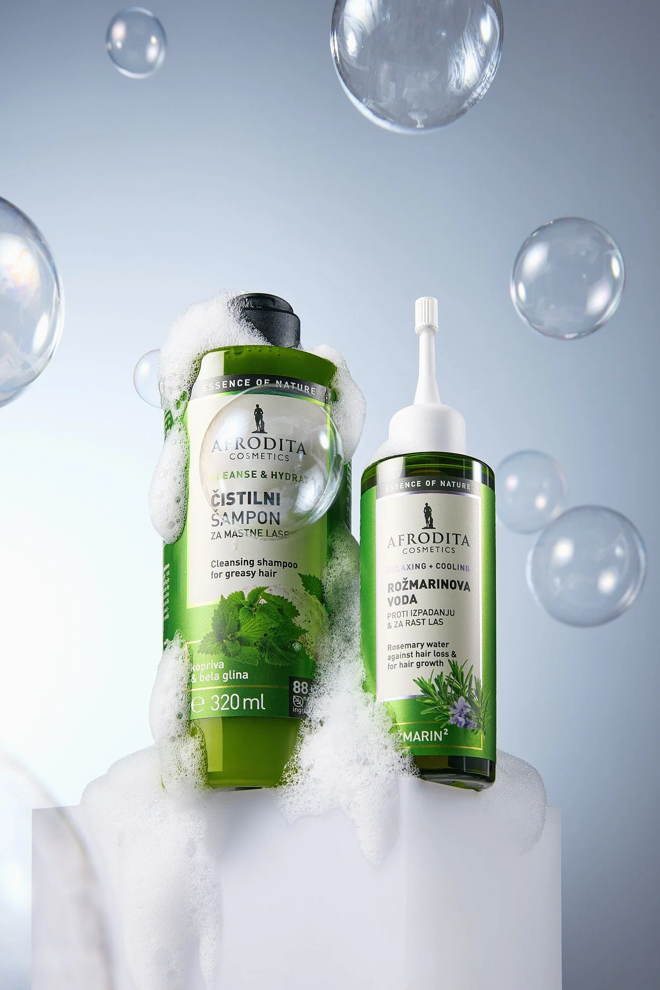 Two green bottles of Afrodita cosmetics products with foam and soap bubbles, set against a light background with floating bubbles.