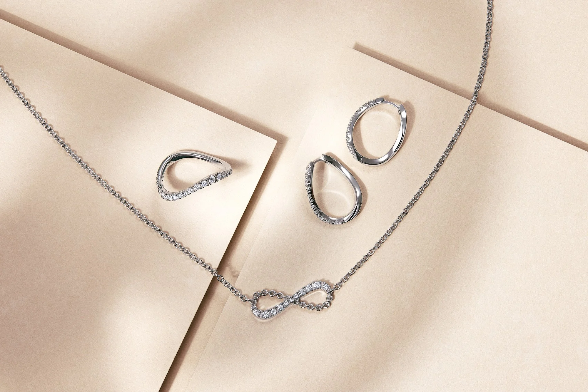Silver jewelry set by Zlatarna Celje including a necklace, a ring, and two rings with diamond embellishments, displayed on beige paper and layered surfaces.