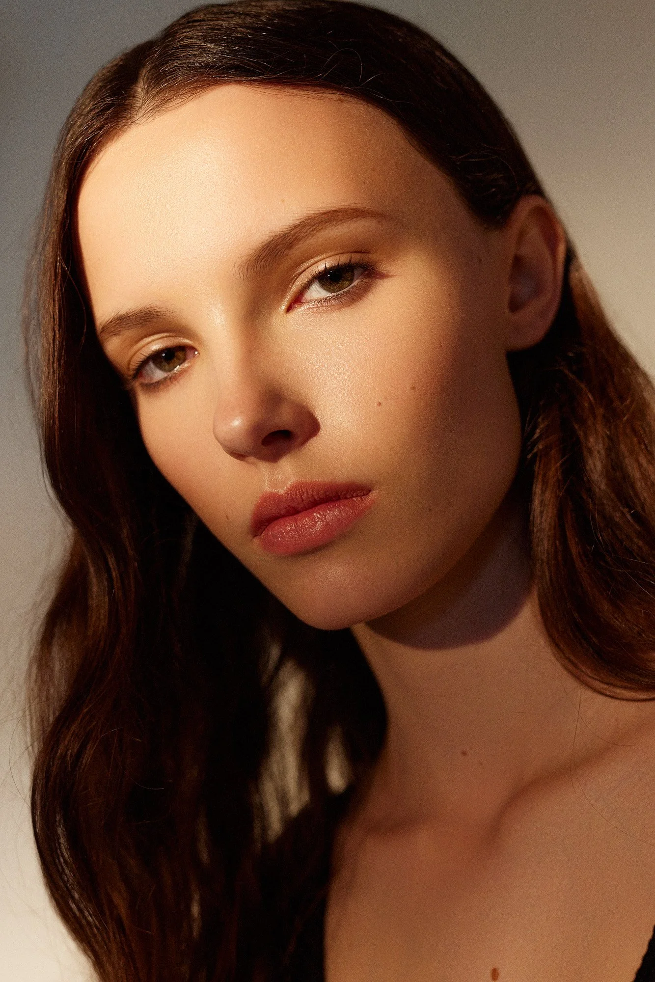 Close-up of a woman's face with long brown hair and light makeup, looking slightly to the side.