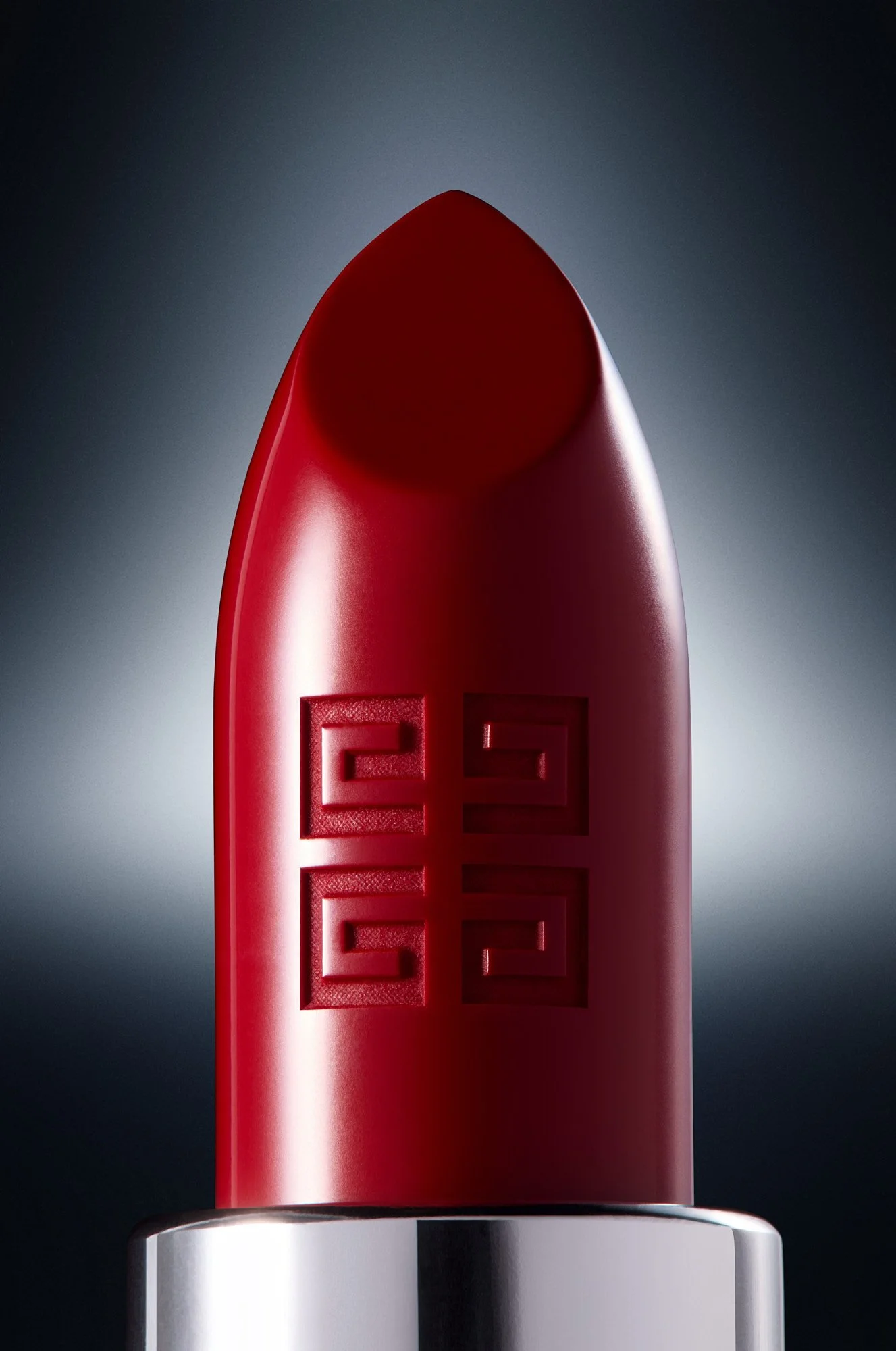 Close-up of a red Givenchy lipstick with embossed brand name on it, set against a dark background with spotlight illumination.